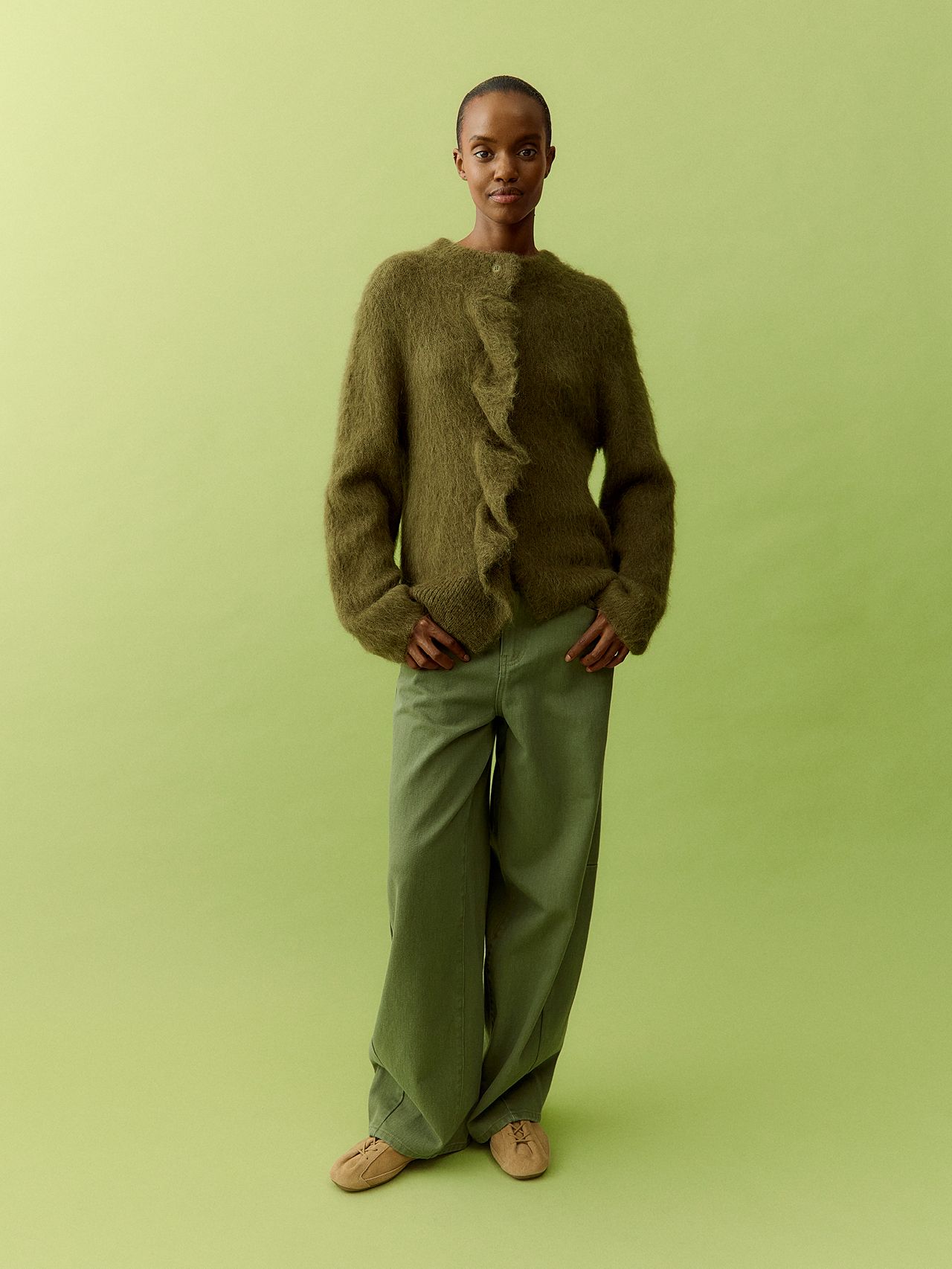 Full-length portrait of a woman in a fuzzy green cardigan and wide-leg trousers