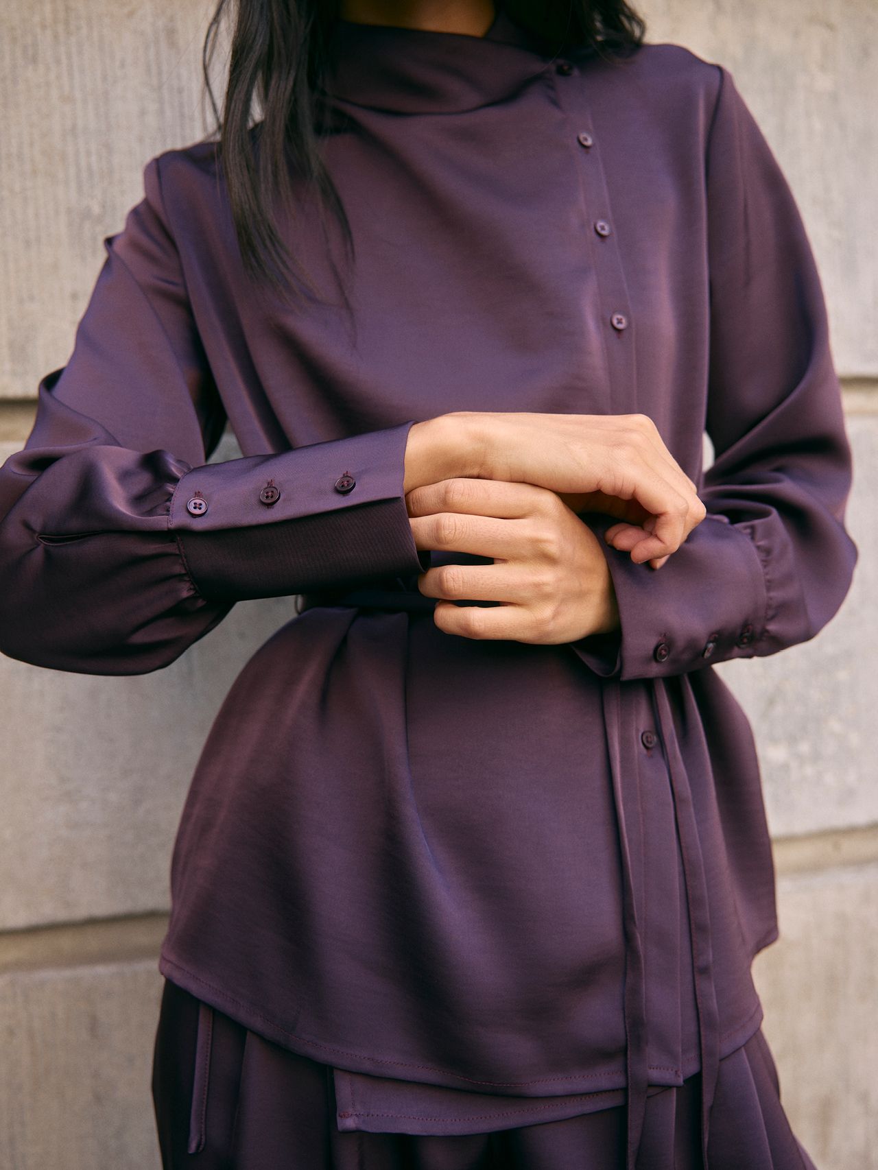 Woman in a plum satin high-neck wrap blouse with buttons, cuffs, and belt