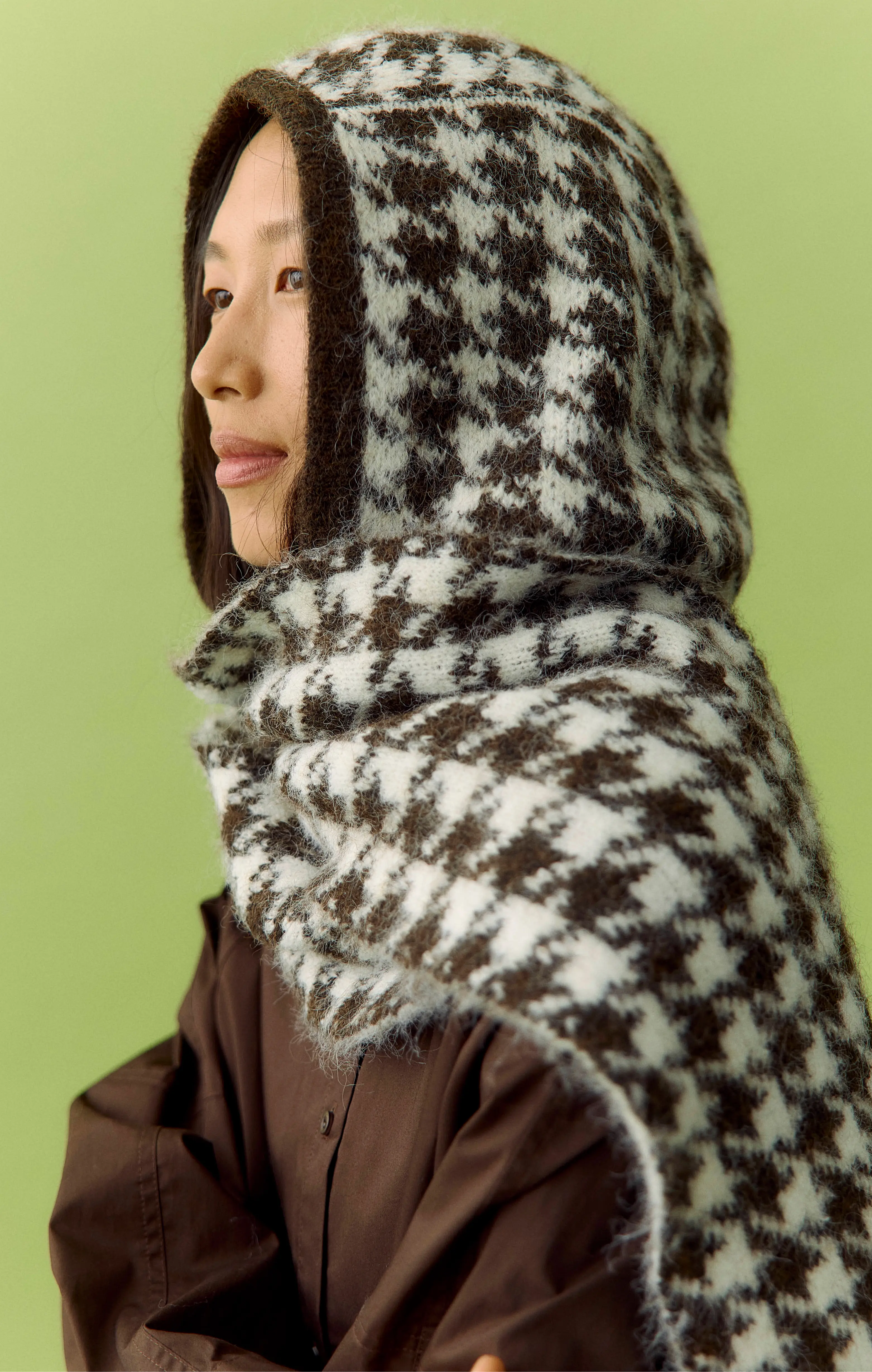 Side profile of an Asian woman in a brown-and-white knitted hood against a green background