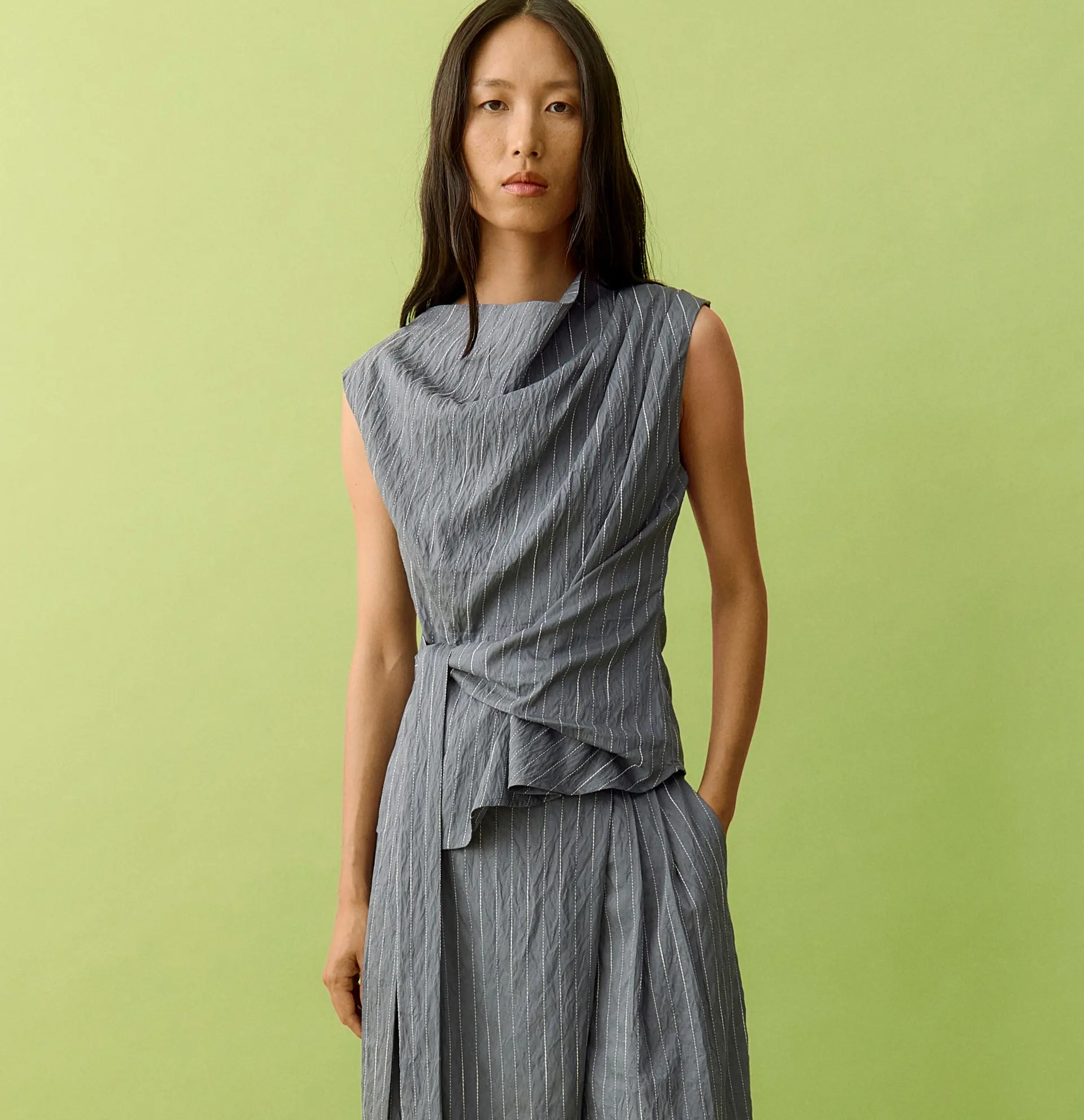 Woman models a grey striped sleeveless top and matching wide-leg pants on green.