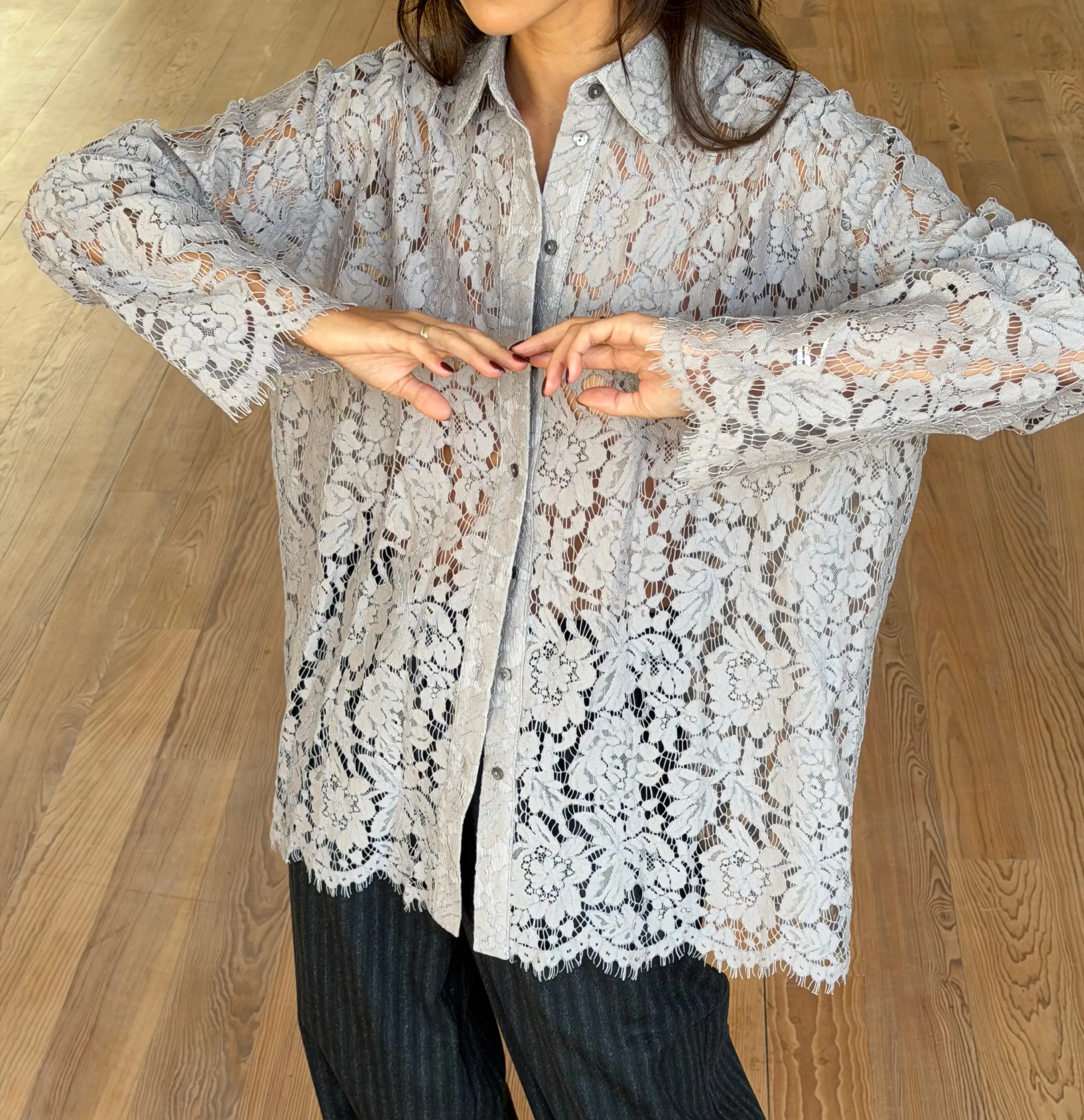 Vrouwelijk model in grijze kanten blouse en gestreepte broek op houten vloer indoors