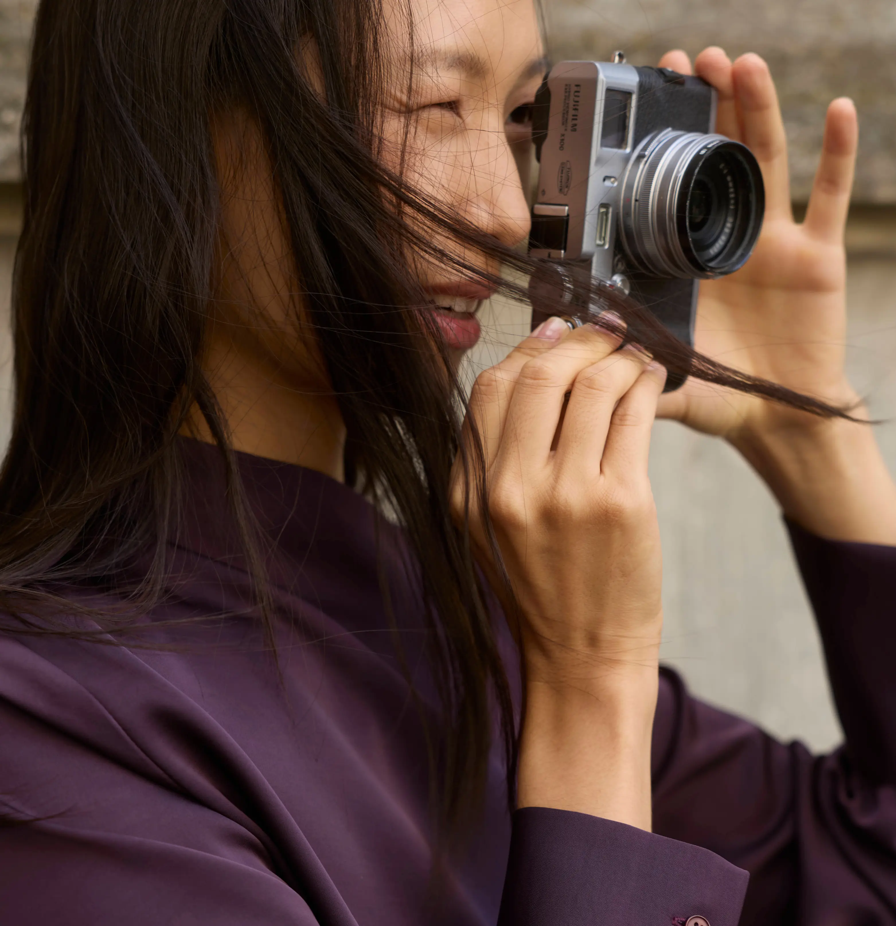 Smiling Asian woman taking a photo outdoors with a Fujifilm mirrorless camera