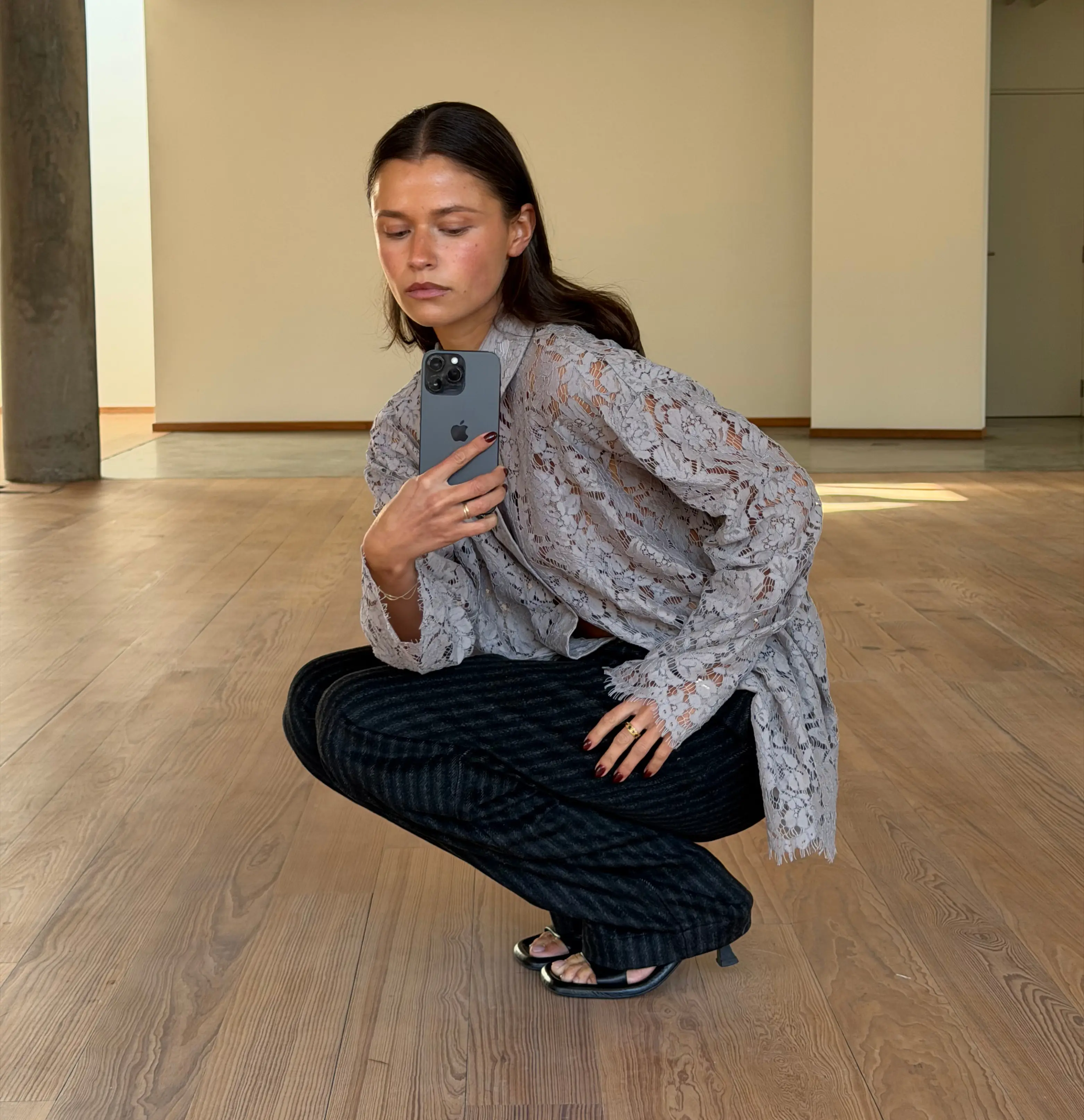 Brunette vrouw hurkt binnen en maakt een selfie in casual outfit met smartphone