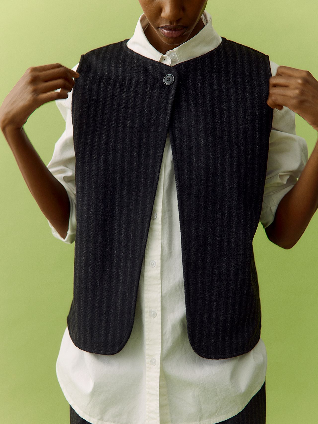 Model in a dark grey pinstriped waistcoat over a white collared shirt on green background