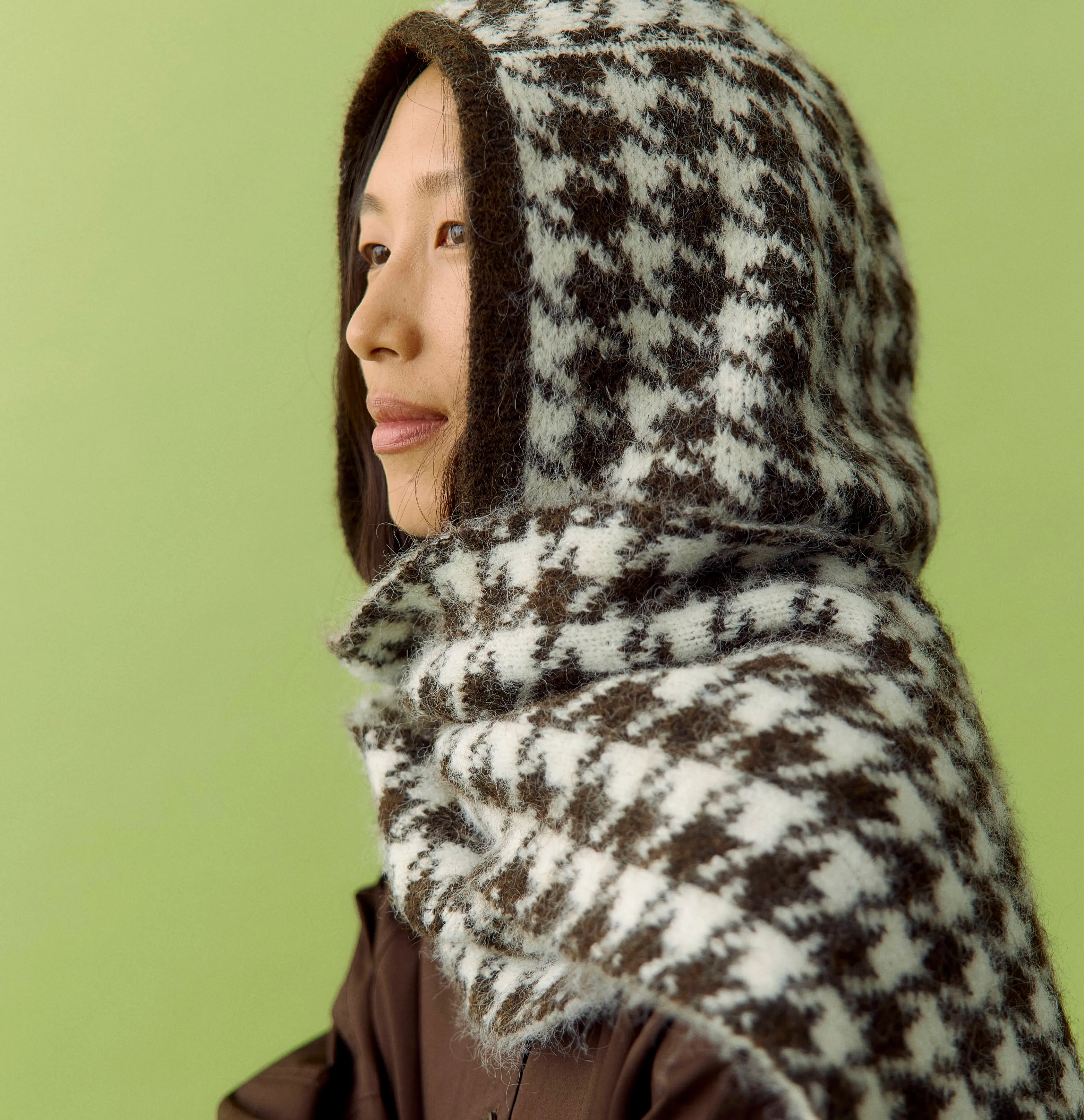 Side profile of an Asian woman in a brown houndstooth knitted hood and scarf.