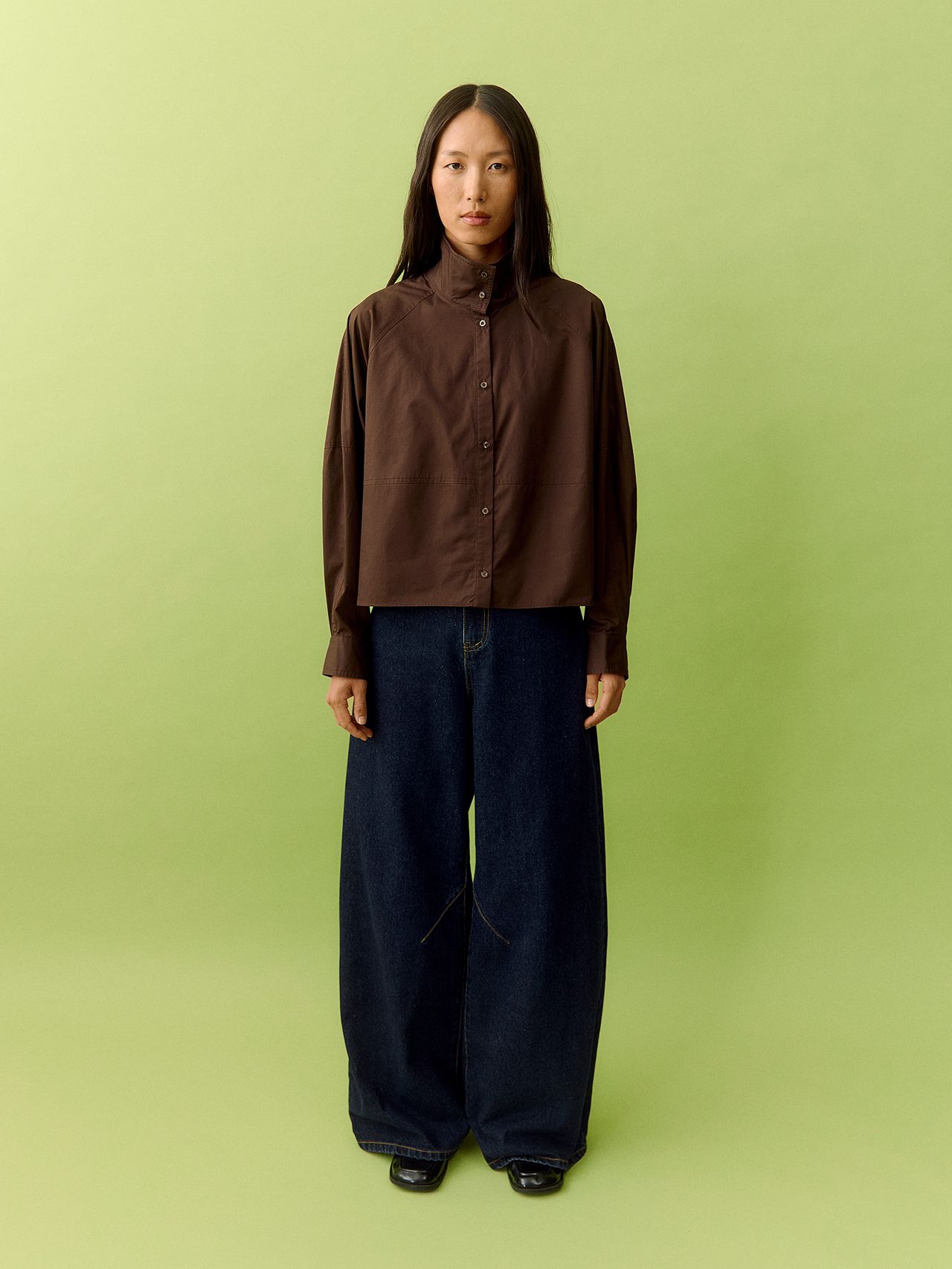 East Asian woman in a brown cropped shirt and wide-leg dark jeans on a lime green backdrop