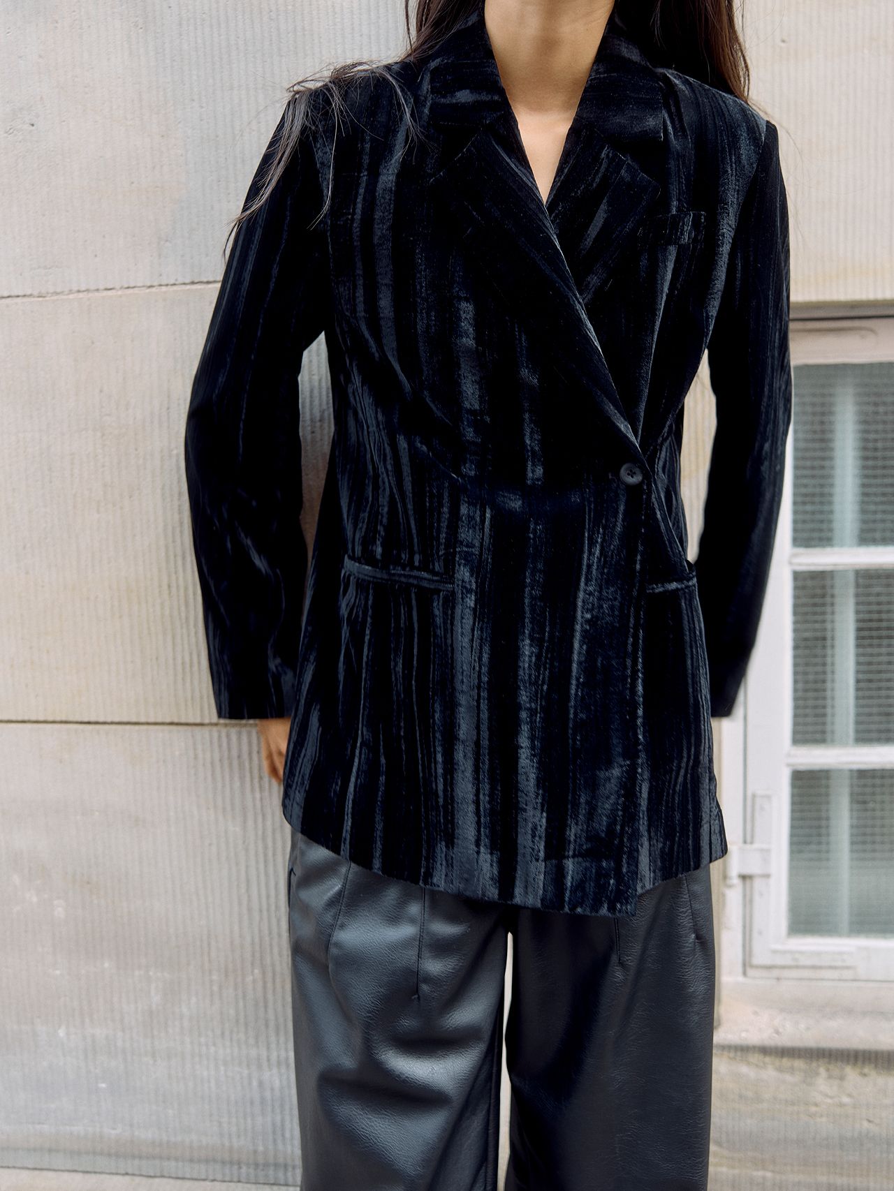 Woman in striped black velvet blazer and leather pants outdoors by a window
