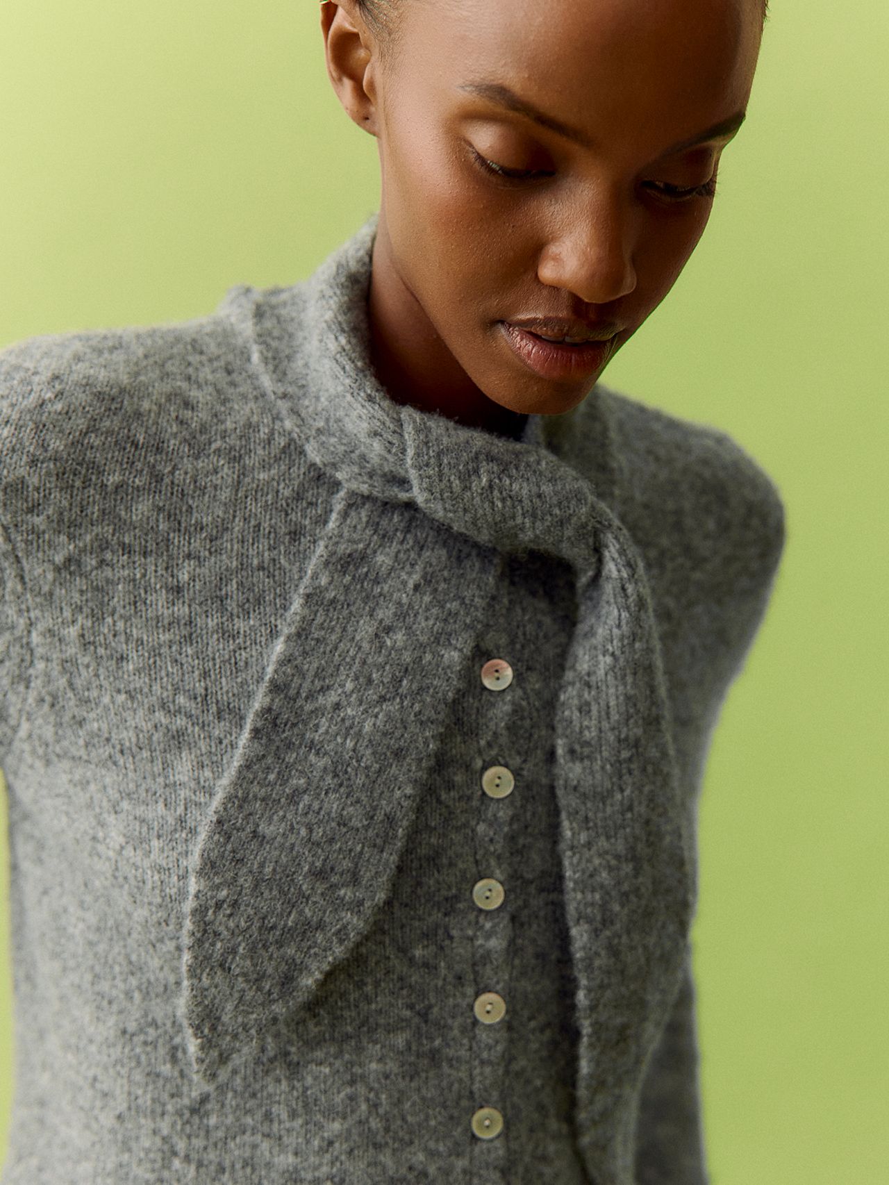Black woman models a heather gray tie-neck knit cardigan against a lime green backdrop