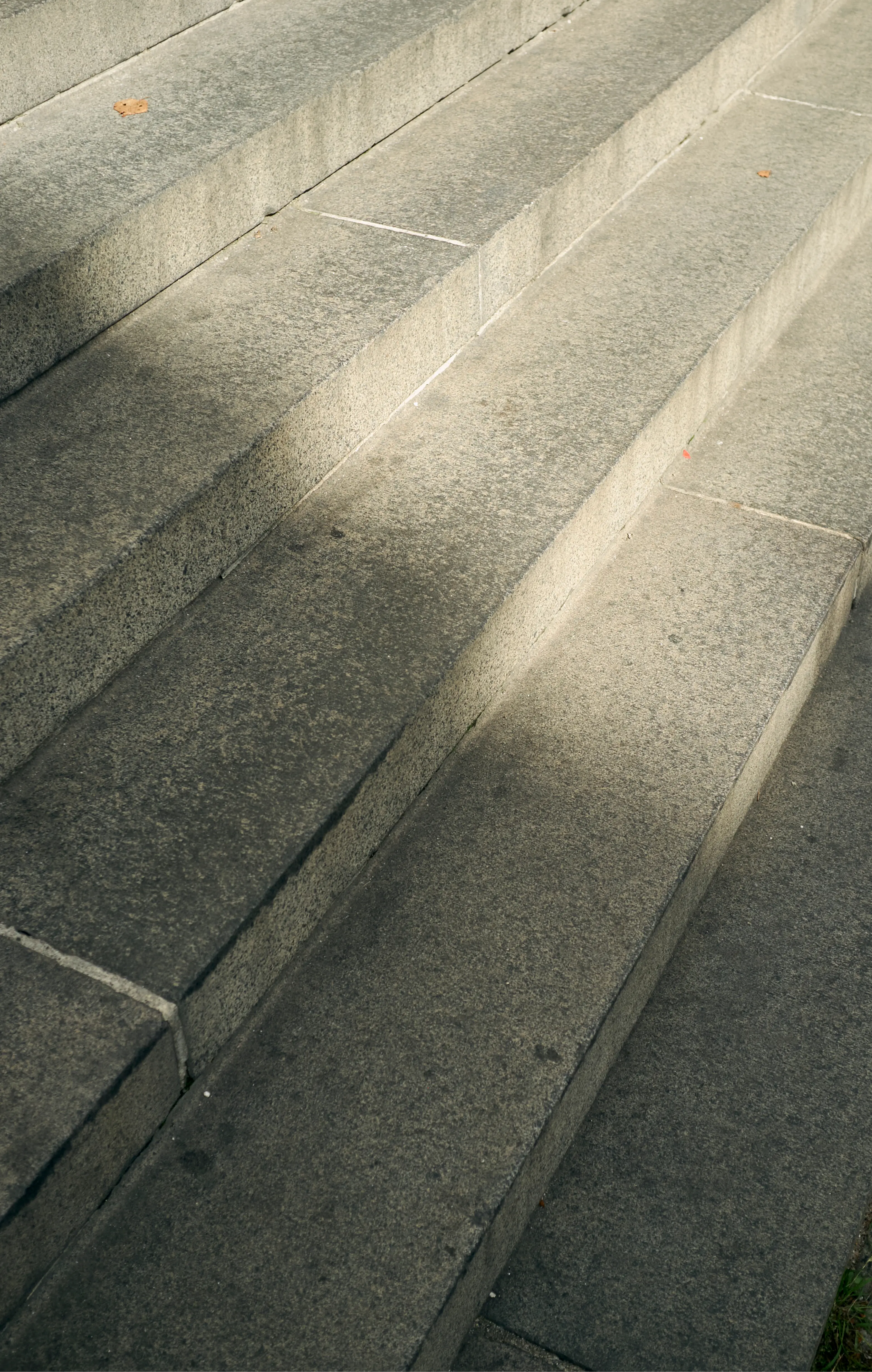Sunlit weathered concrete steps with diagonal shadows and a fallen leaf