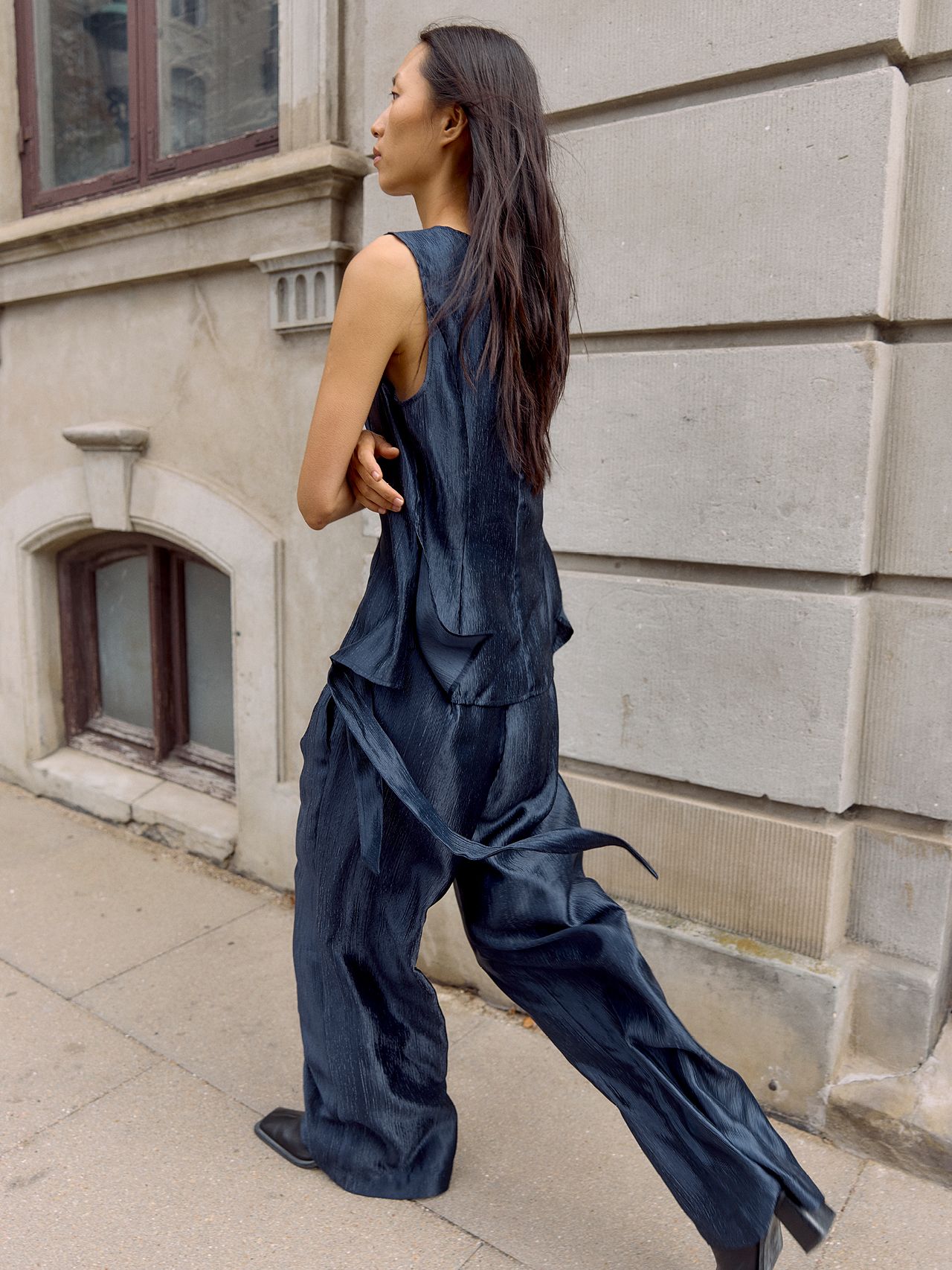 Asian woman in a navy textured set and black shoes walking on a city street.