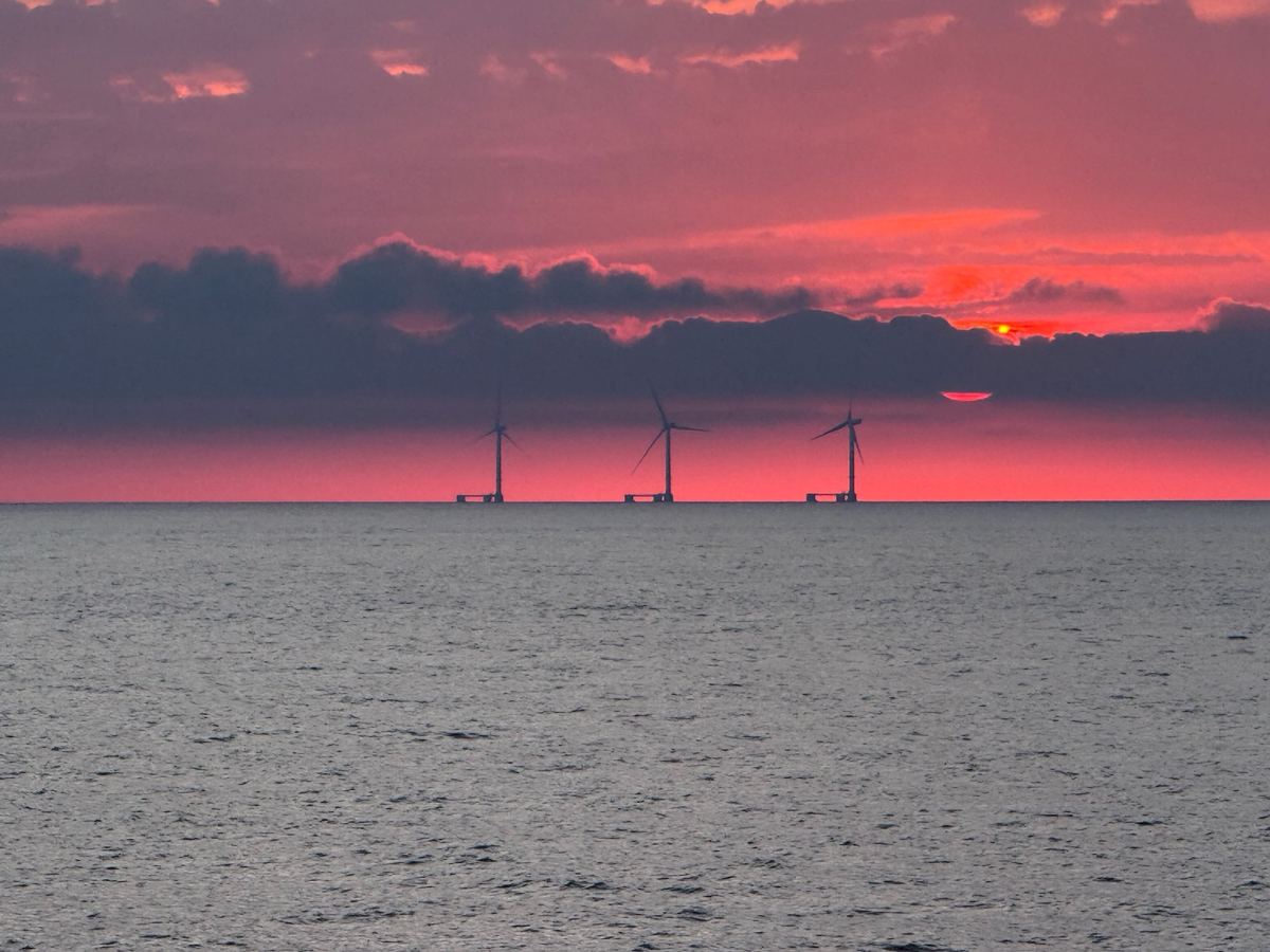 Floating offshore wind turbines silhouetted against a red sunset