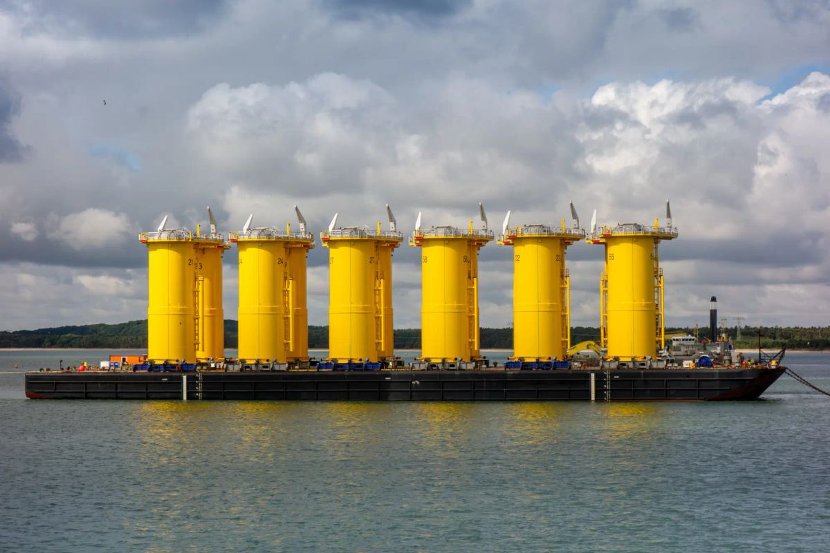 Offshore wind foundations loaded on a barge, seen side on