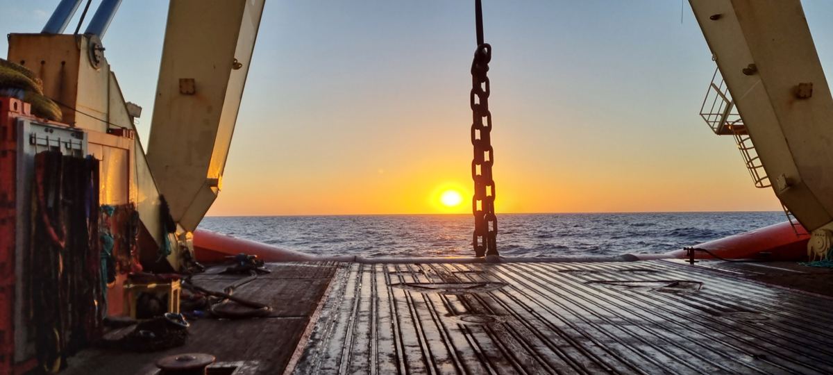 Lifting chain over the open working deck of an offshore vessel at sunrise