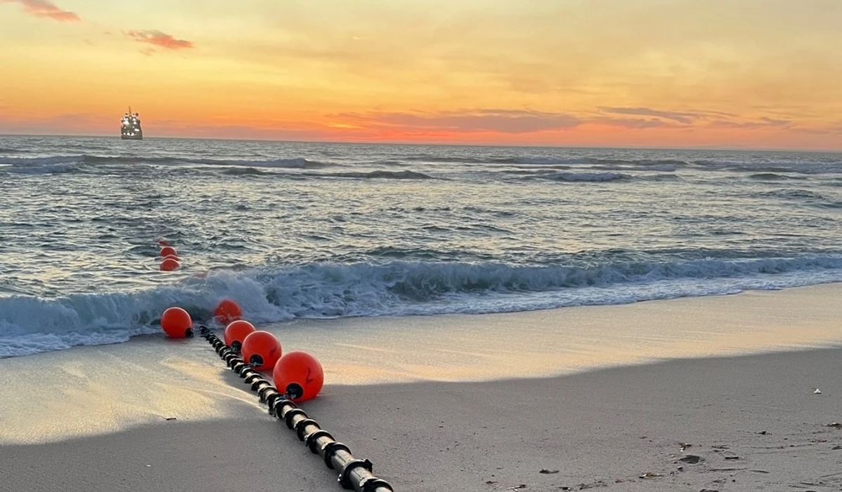 Subsea cable brought ashore across a beach at sunset, floated in on red buoys, with a vessel on the horizon