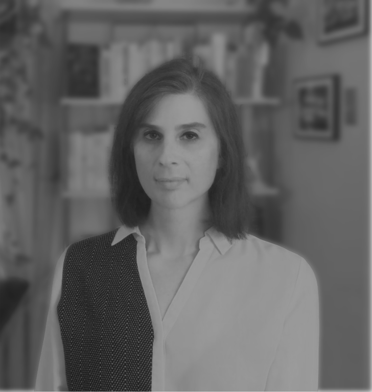Portrait of Maddie Nielsen wearing a white and black-patterned color blocked collared blouse with a bookshelf, plants, and frame photographs in the background