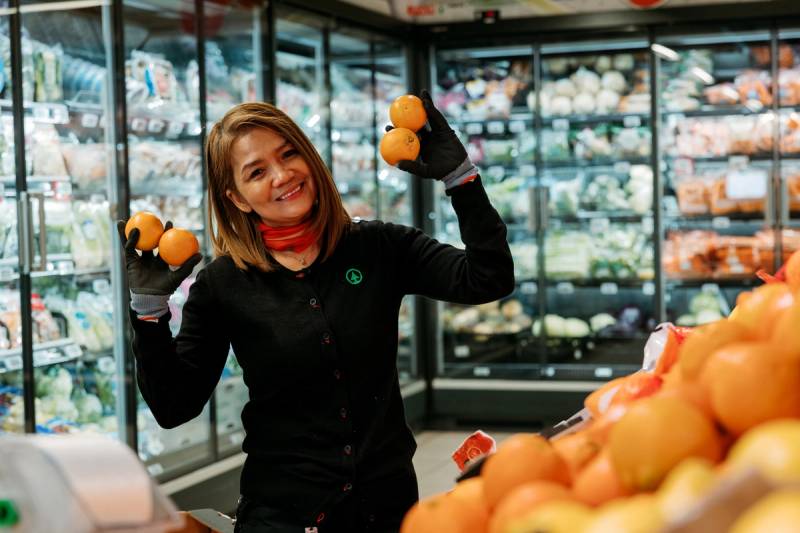 En SPAR-ansatt som er smilende og holder opp klementiner i hånden
