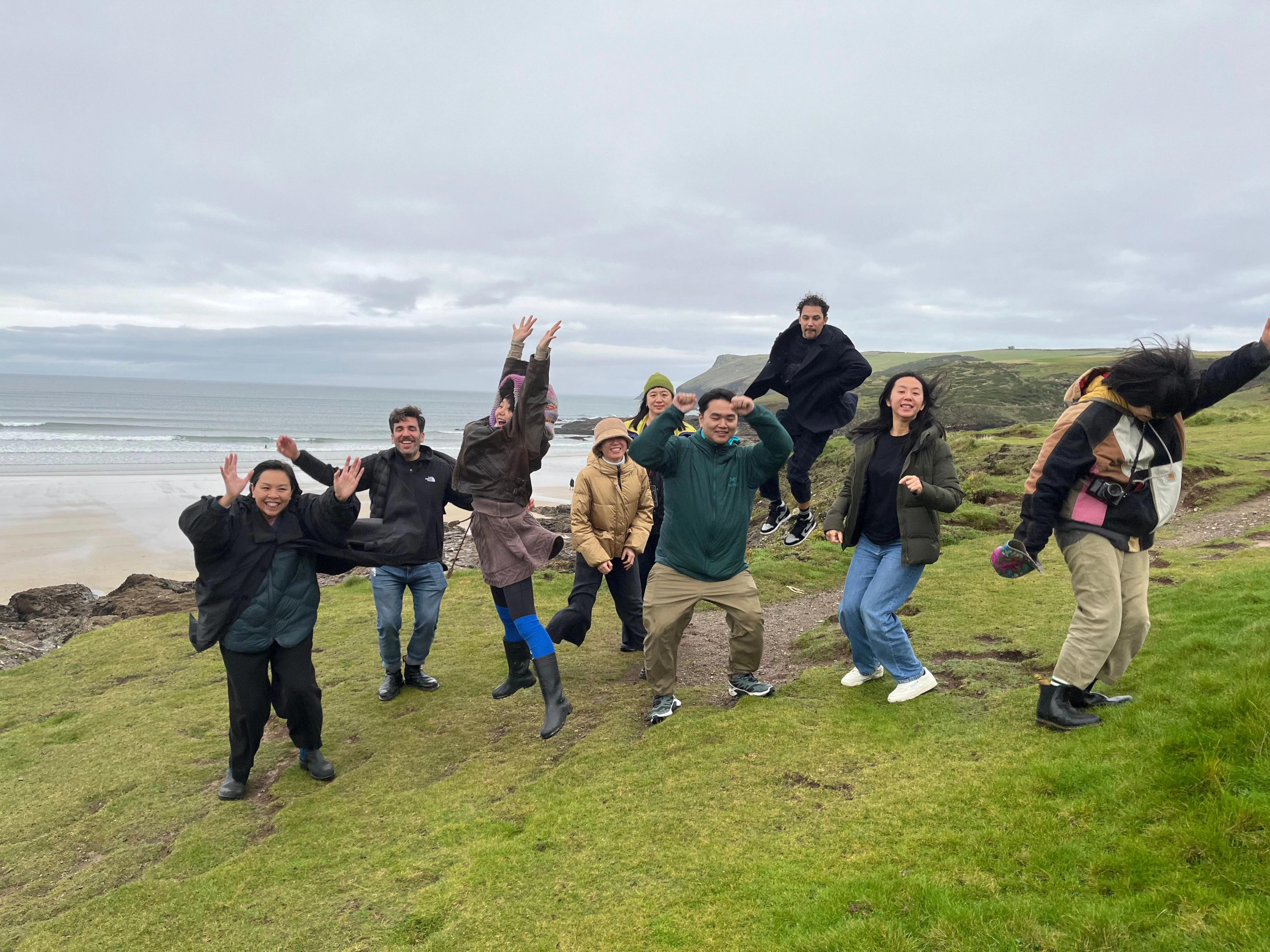 BAO team jumping on grassy cliff by the ocean on a cloudy day