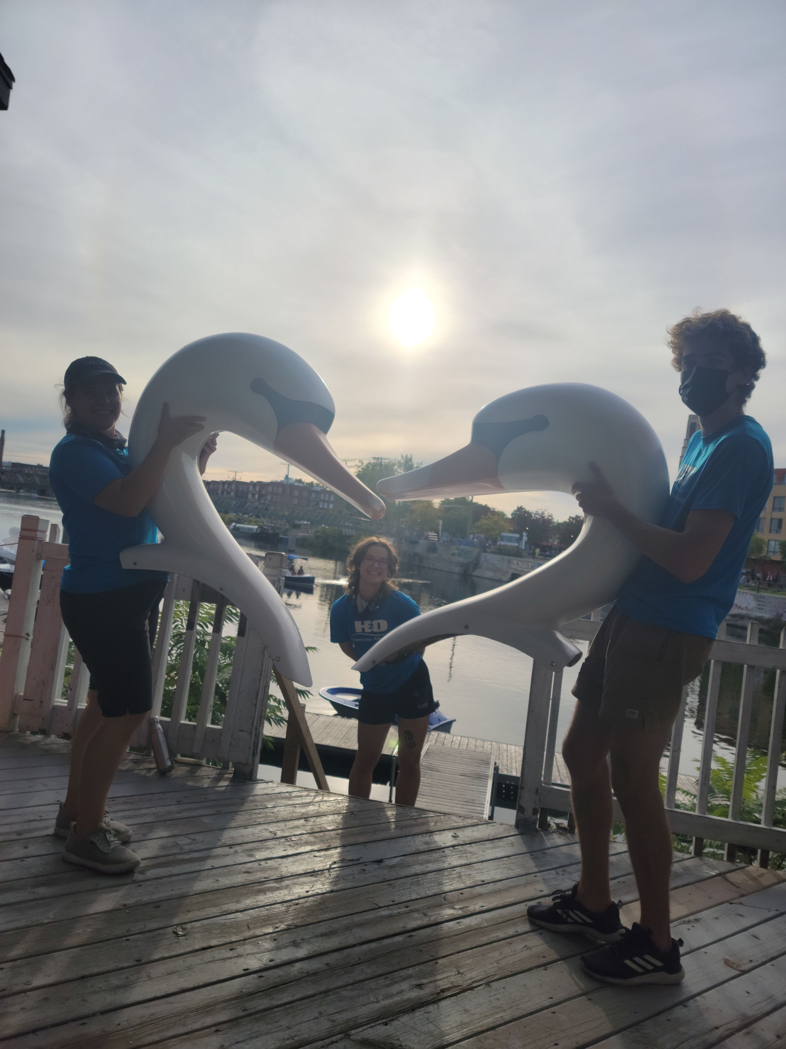H2O Adventures staff members holding swan paddle boat heads on the dock at sunset along the Lachine Canal in Montreal.