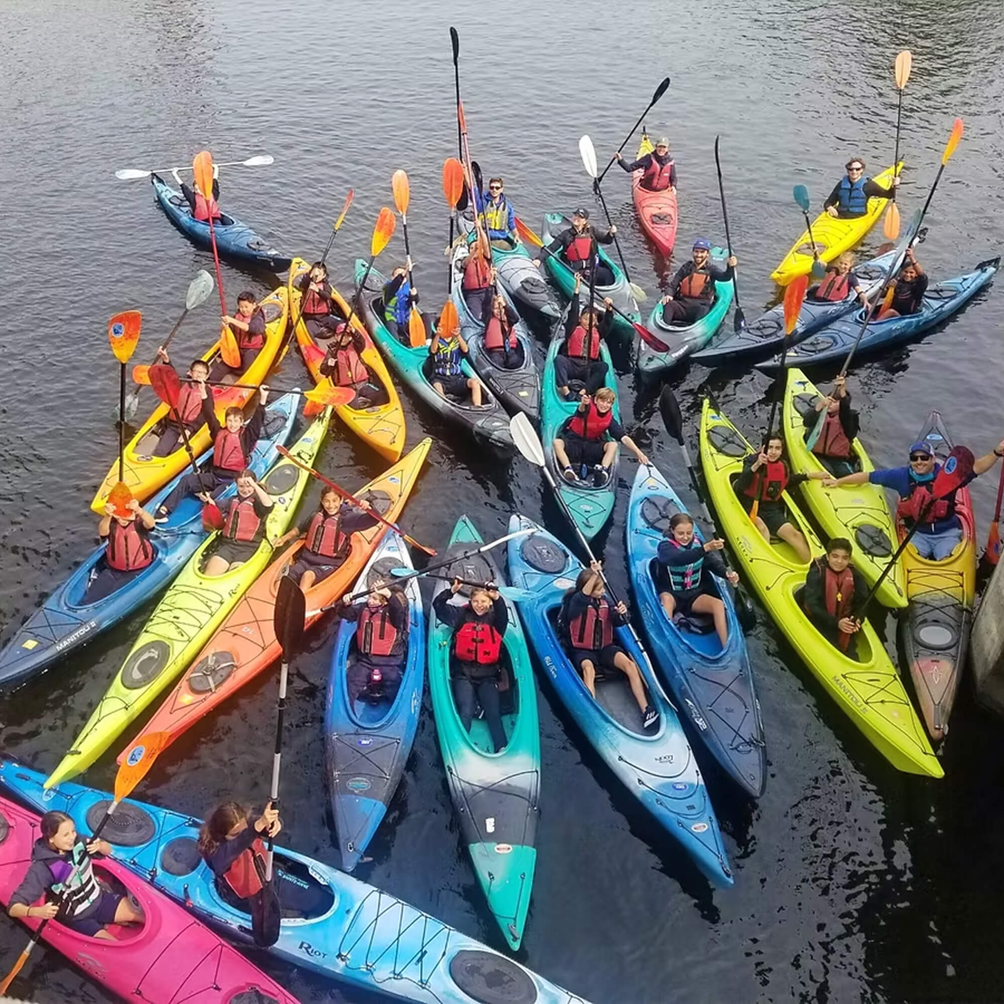 A large group of kayakers gathered on the water, smiling and posing for the camera on the Lachine Canal in Montreal.