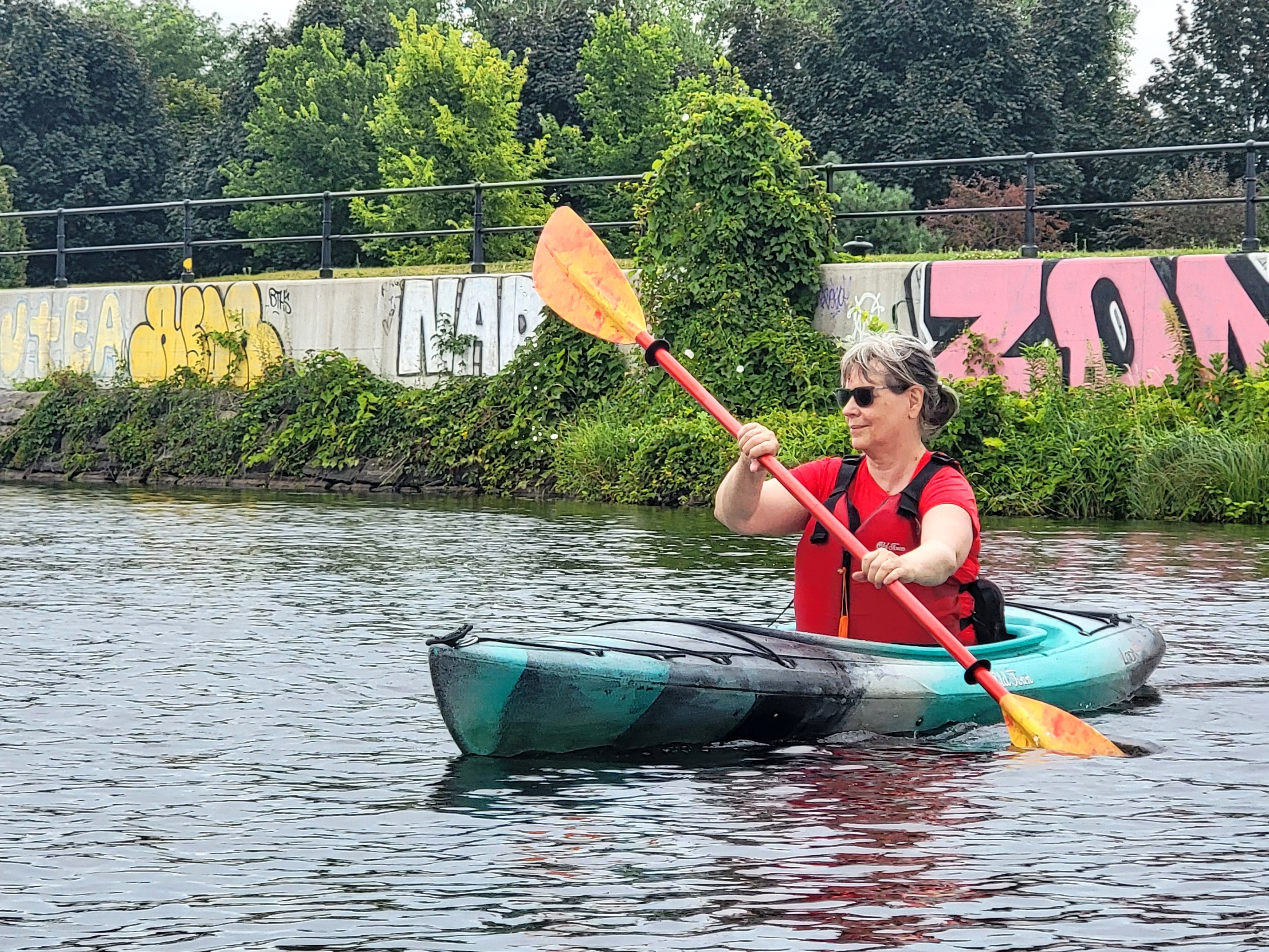 A close-up shot of an older woman smiling as she paddles her kayak along the Lachine Canal in Montreal.
