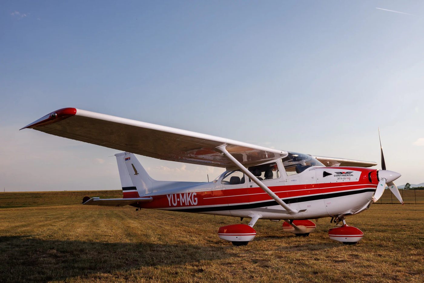 Crveno-beli avion Cessna na travnatoj površini aerodroma