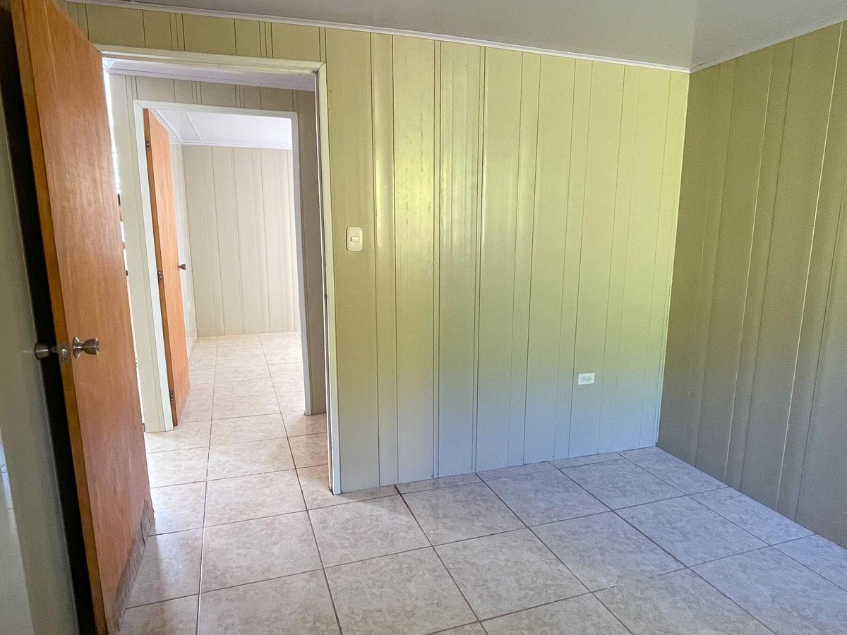 Un cuarto vacío de la casa modelo, paredes verde olivo y la puerta abierta al pasillo.