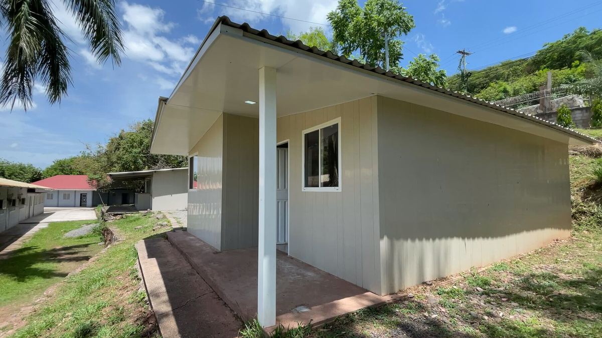 La esquina de la casa modelo, con su corredor y el cerro verde detrás.