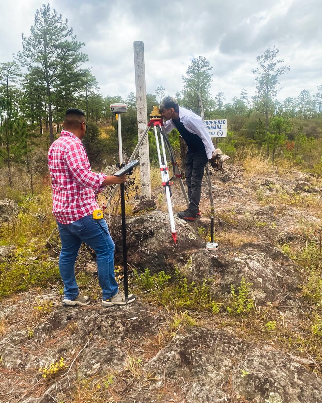 Dos topógrafos trabajando con un teodolito montado en trípode sobre el terreno del proyecto.