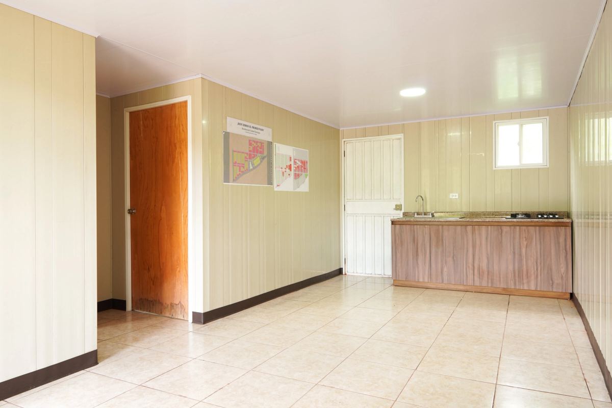 La sala y la cocina de la casa modelo vistas desde el pasillo: paredes beige, piso de azulejo y gabinete de madera.
