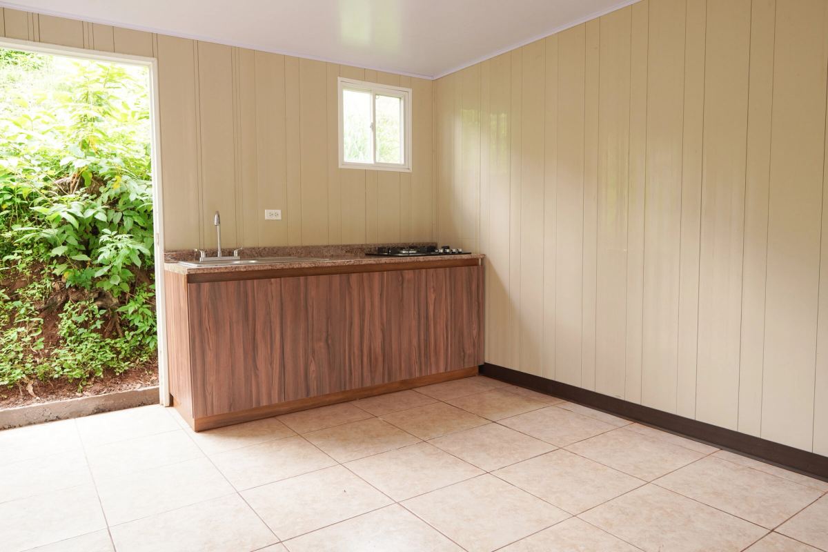 La cocina de la casa modelo con su gabinete de madera, y la puerta abierta al verde del cerro.