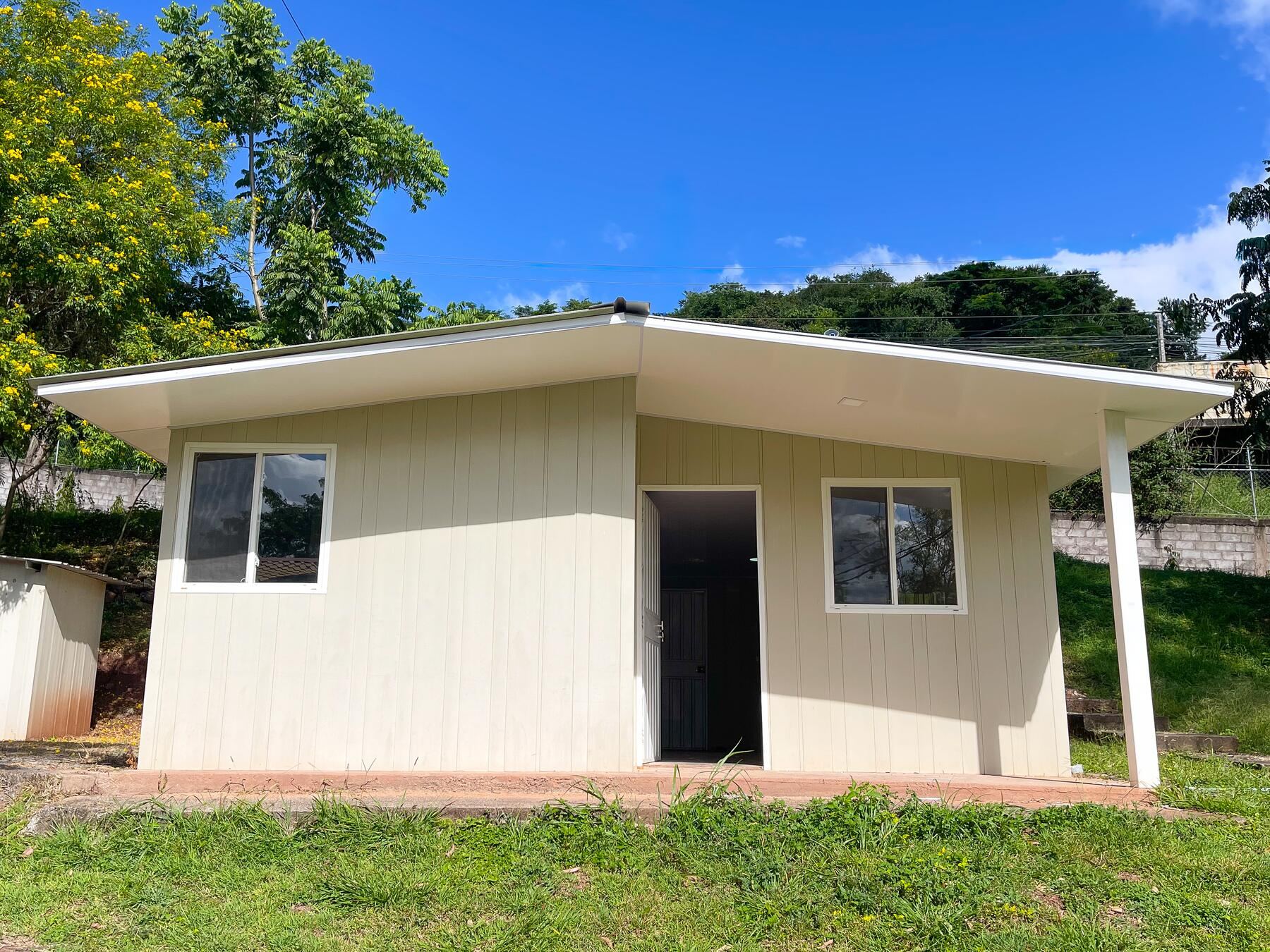La casa modelo vista de frente: paredes de tabla beige, techo de zinc y cielo despejado.