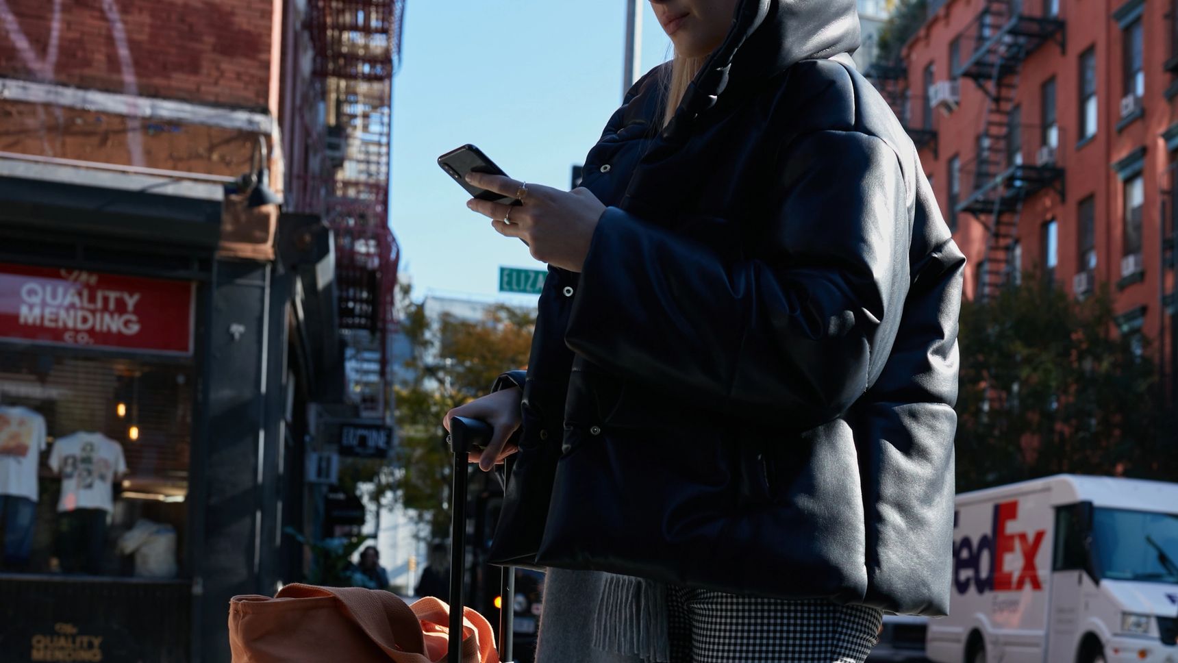 A woman in the streetscape looking at her phone. In her other hand, she holds her rolling suitcase.