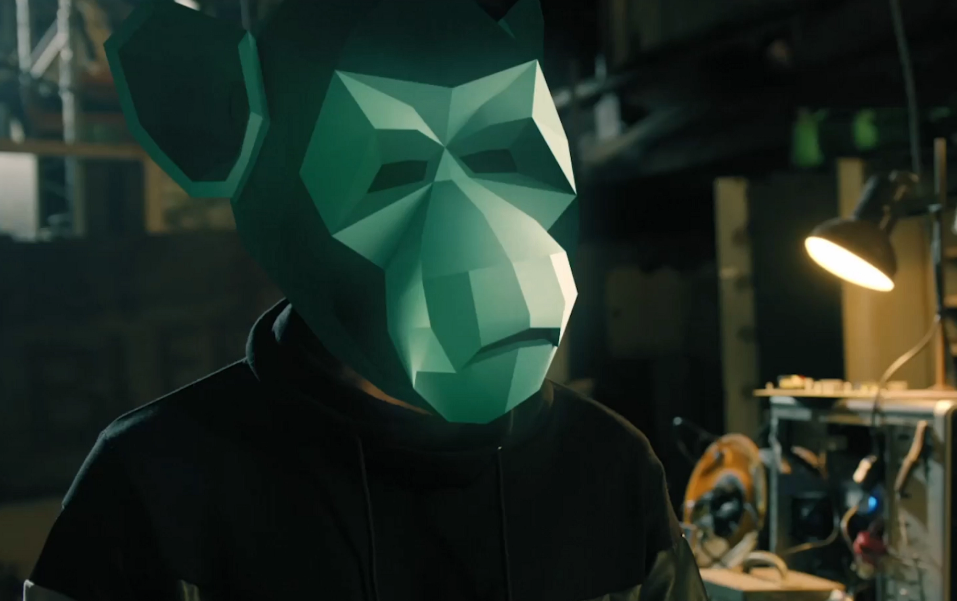 Person wearing a green monkey mask standing inside an industrial workplace.