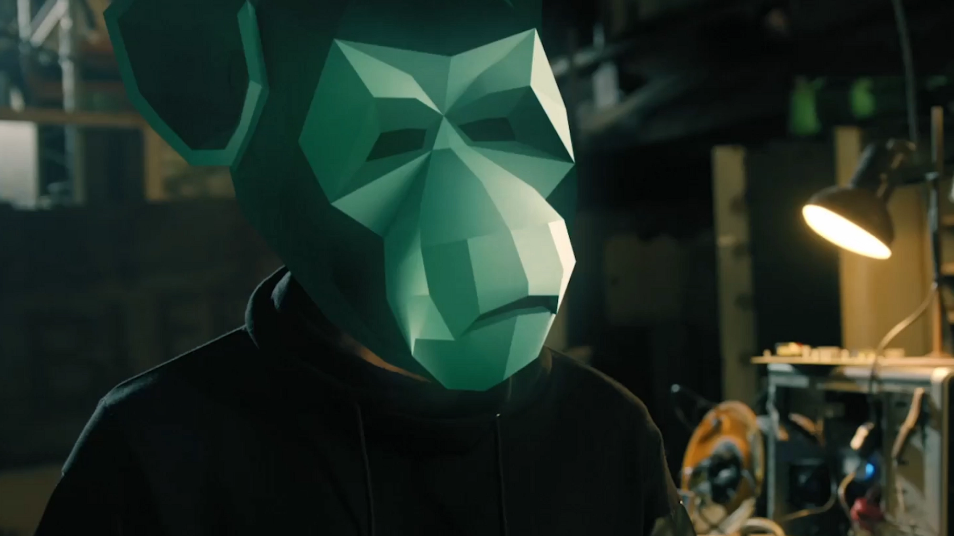Person wearing a green monkey mask standing inside an industrial workplace.