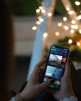 Back view of a woman holding a mobile device. The screen displays the mobile app home screen of NewsON consisting of news items.