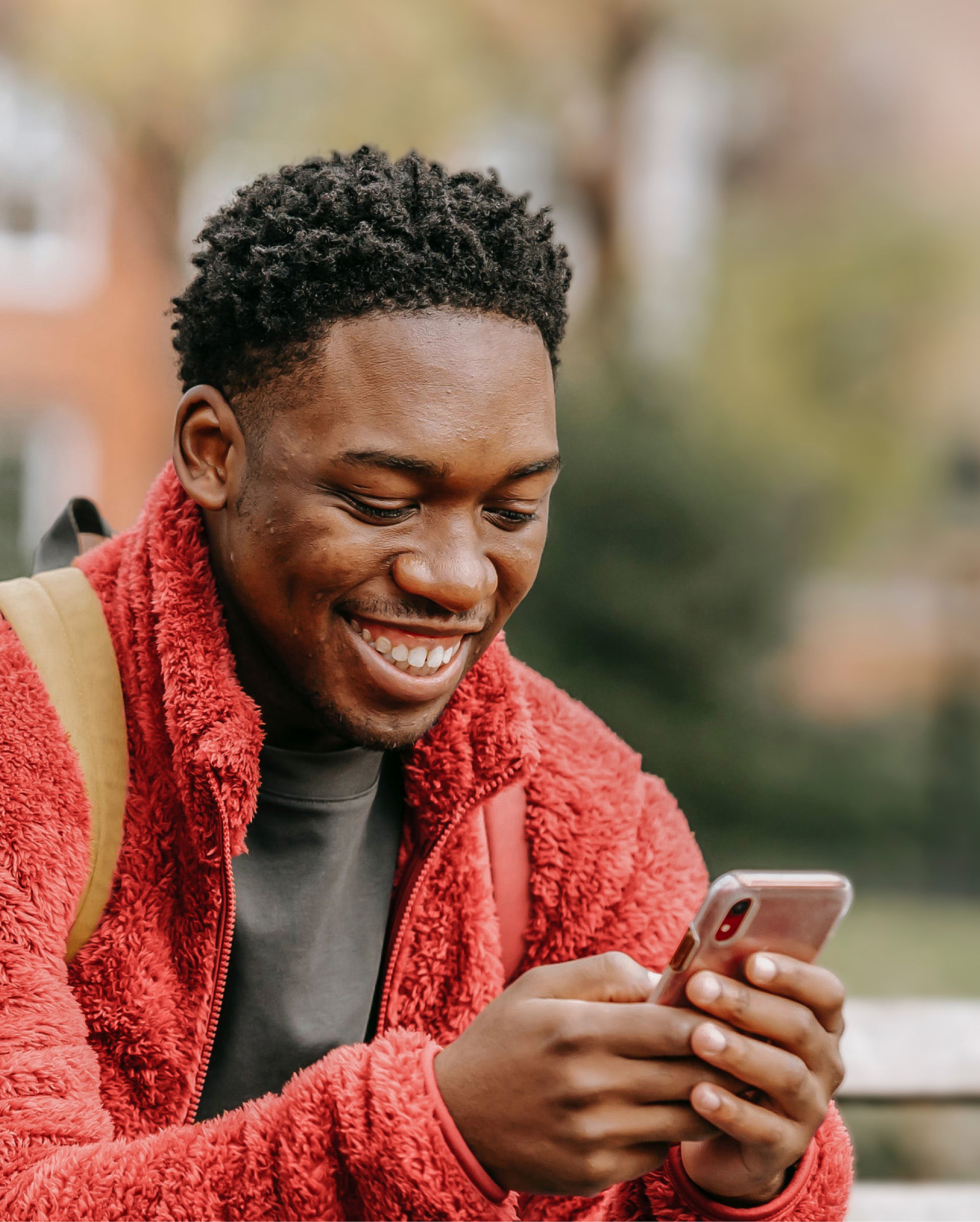 A smiling man looking at his phone in a park.