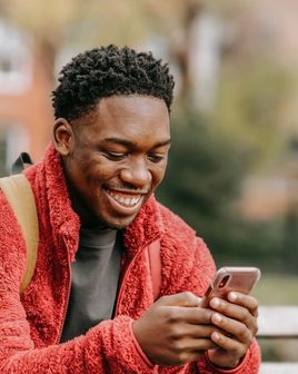 A smiling man looking at his phone in a park.