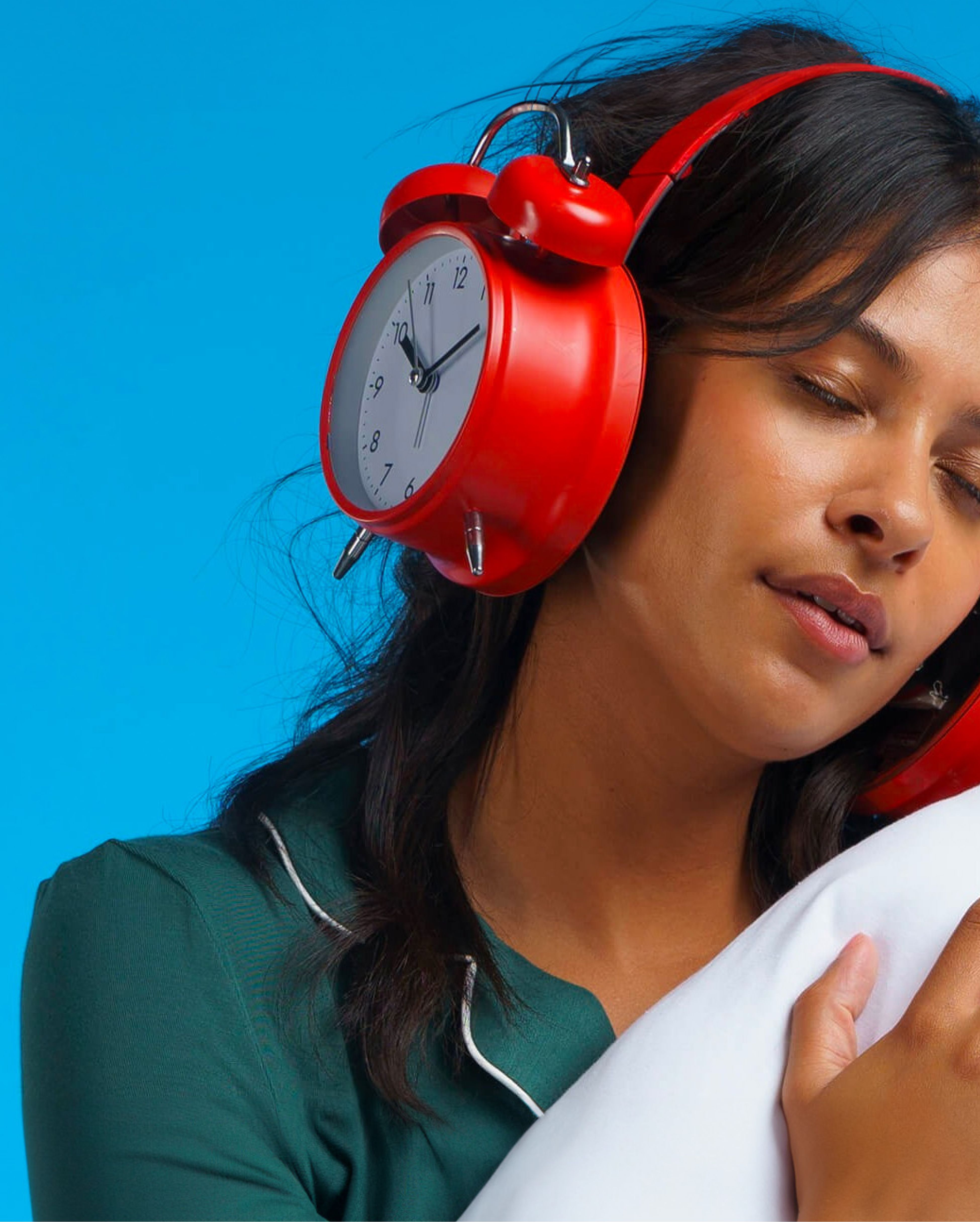 A woman with her eyes closed holding a pillow. Her over-ear headphones are shaped like analog alarm clocks.