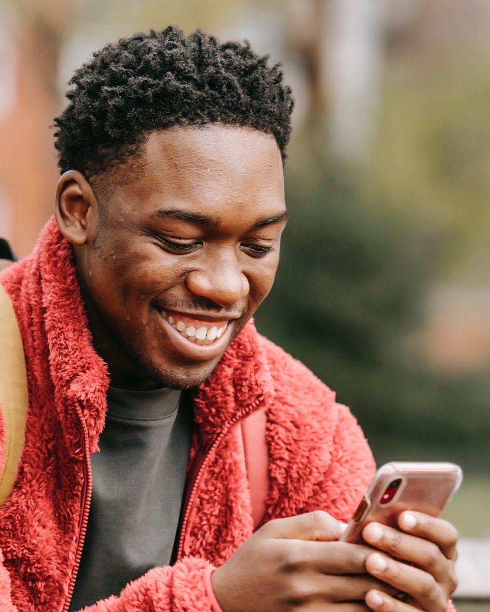 A smiling man looking at his phone in a park.