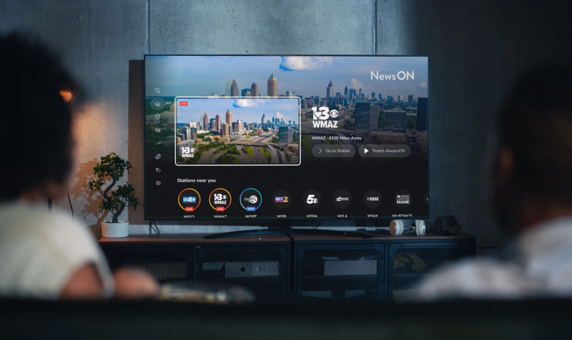 Living room setting with two people watching their smart TV. The smart TV displays the home screen of the NewsON connected TV app.