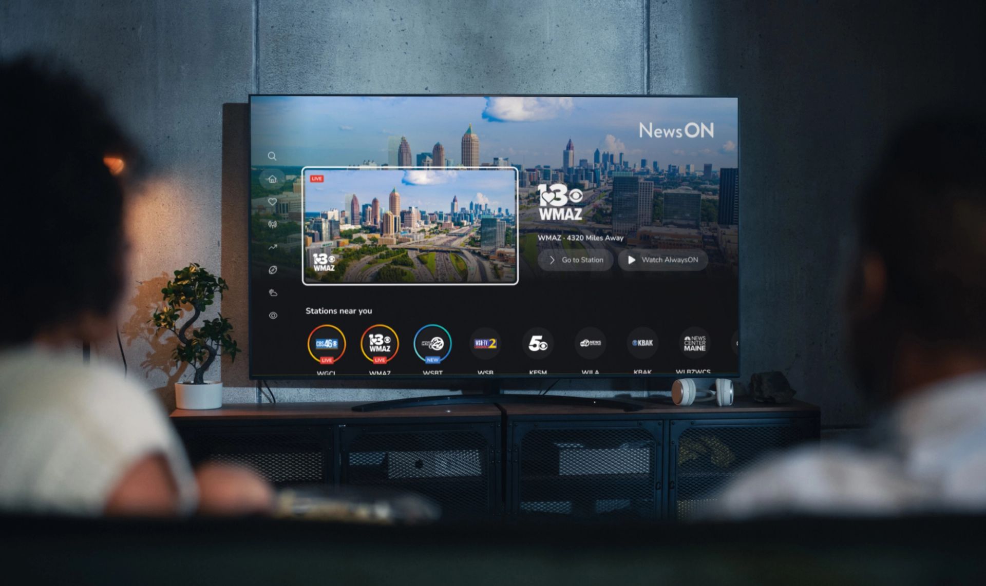 Living room setting with two people watching their smart TV. The smart TV displays the home screen of the NewsON connected TV app.