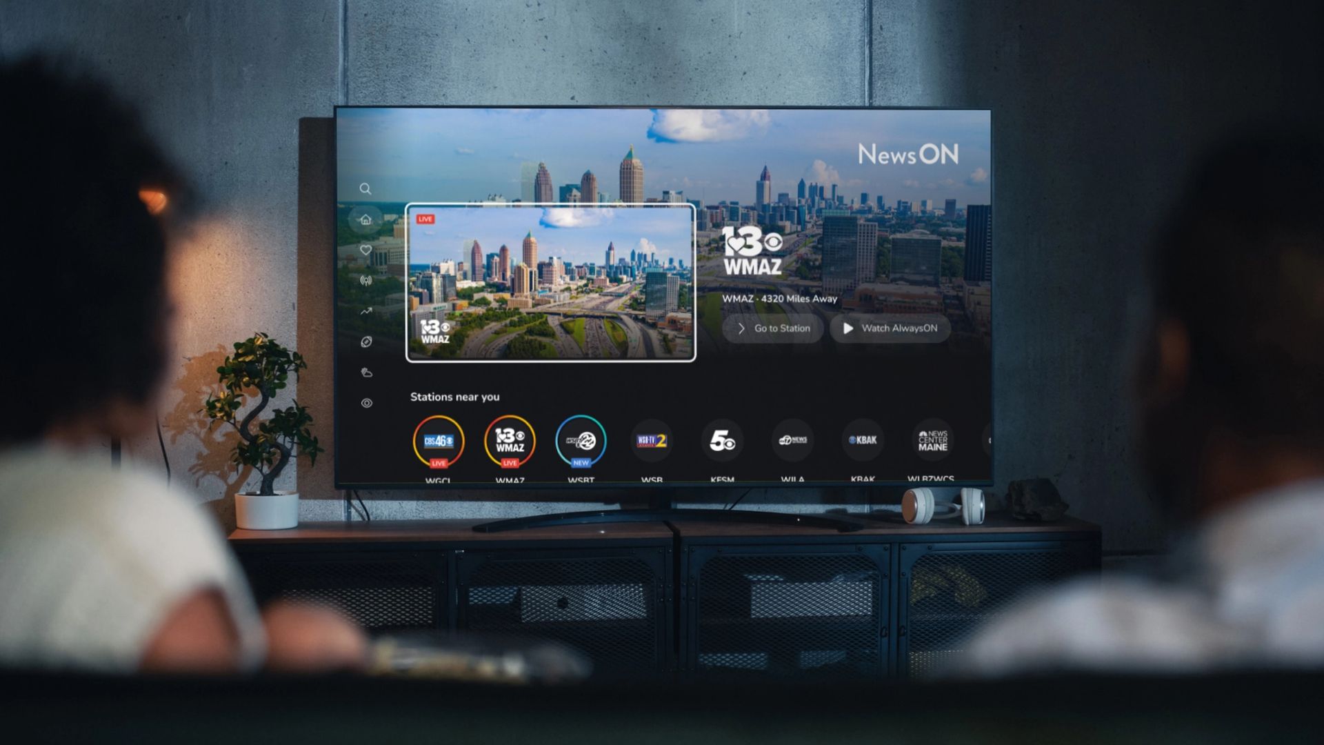 Living room setting with two people watching their smart TV. The smart TV displays the home screen of the NewsON connected TV app.