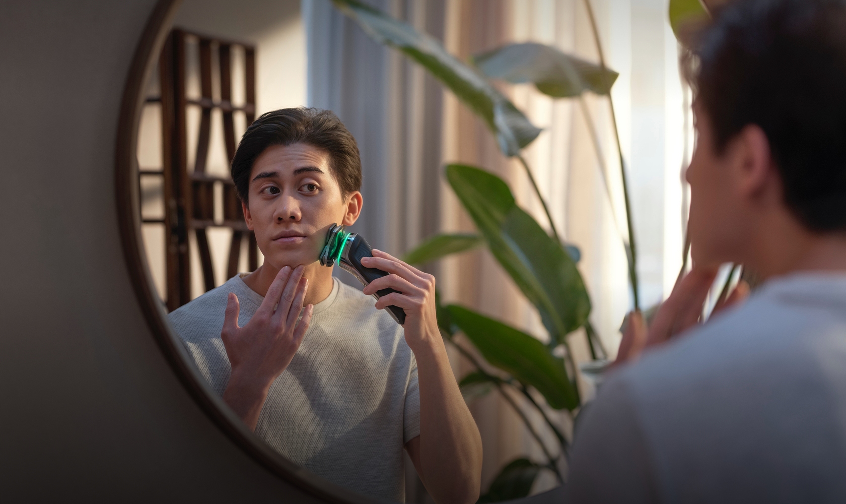 A man shaves in front of a mirror using his Philips electric shaver.