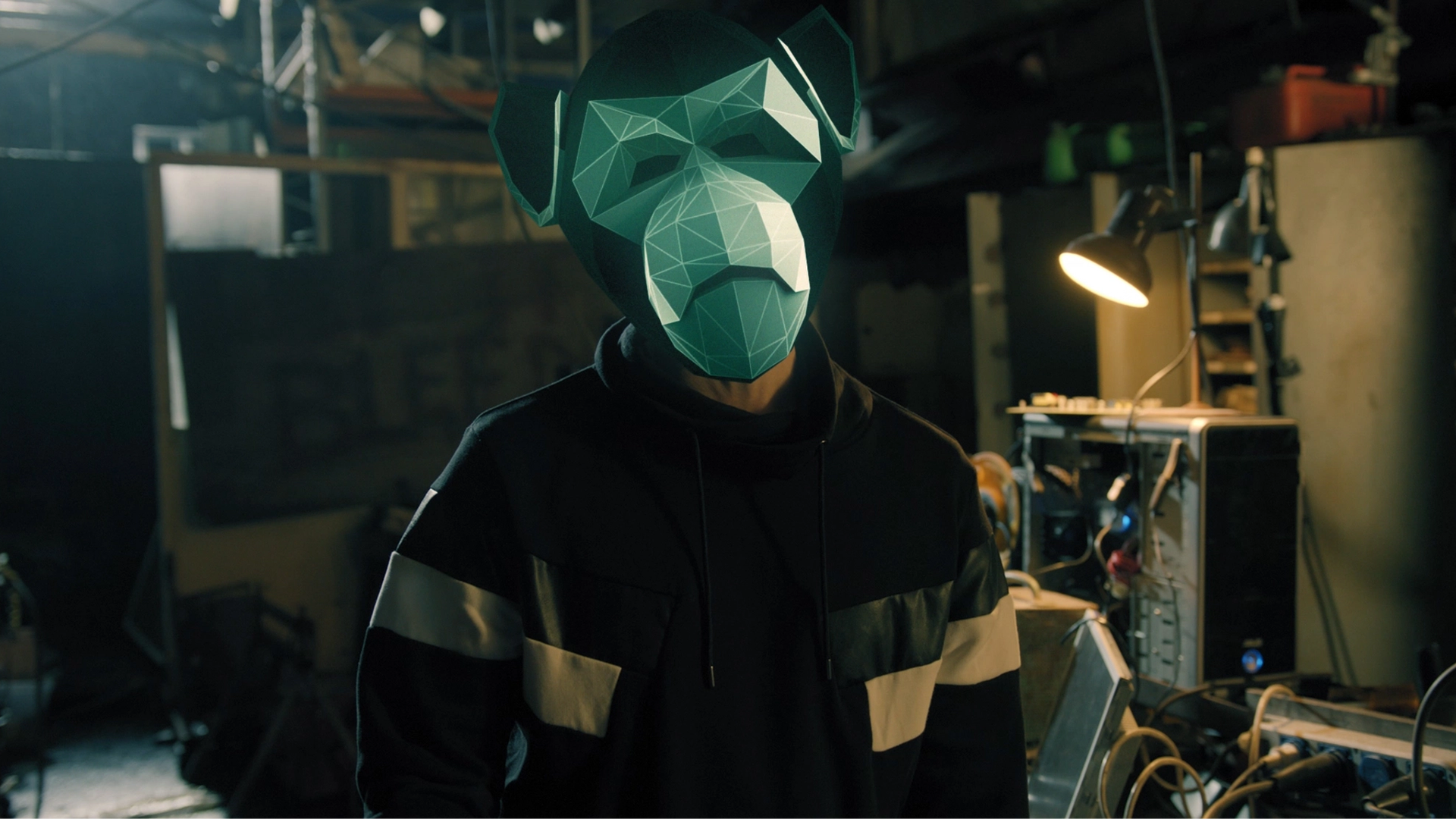 Person wearing a green monkey mask standing inside an industrial workplace.