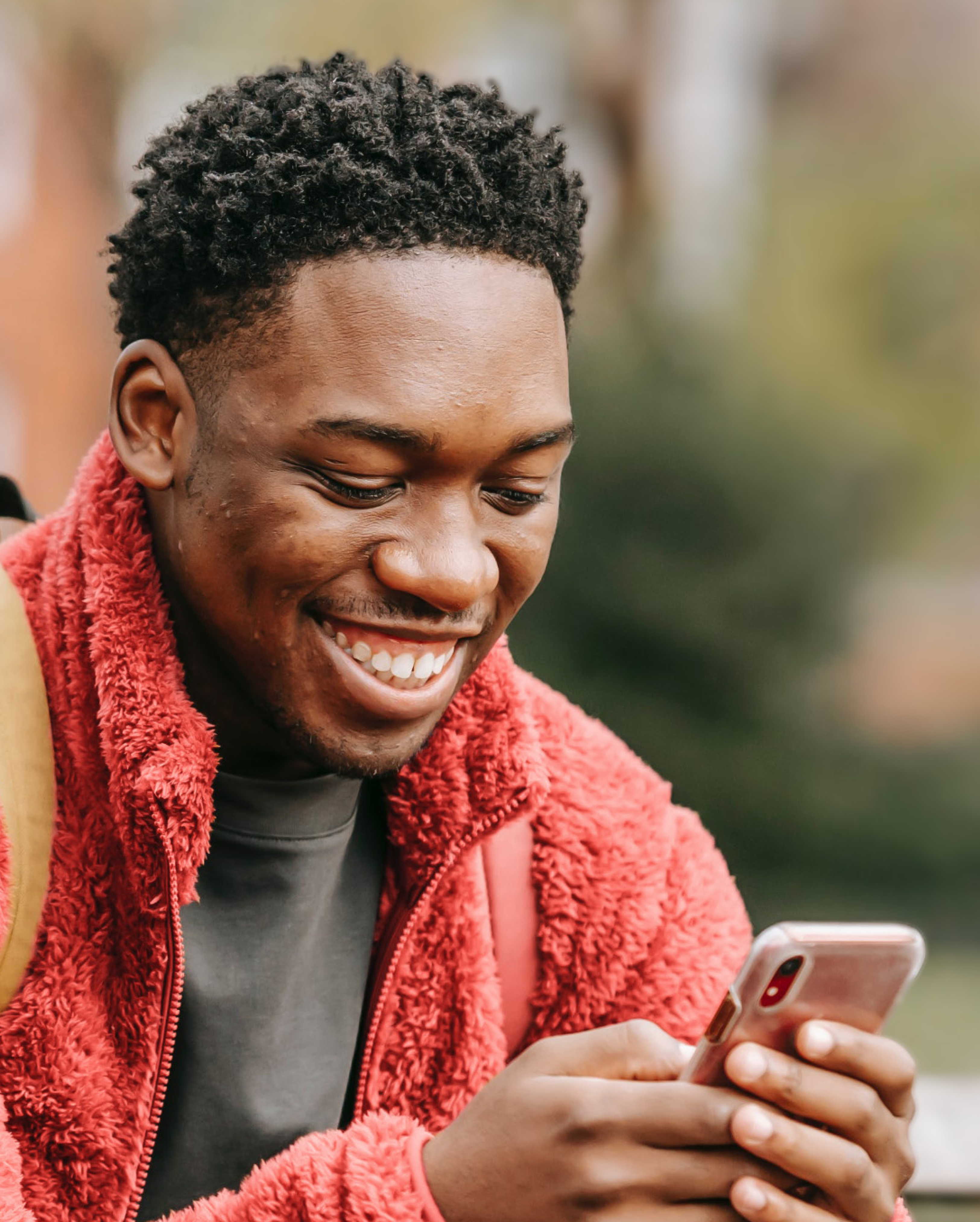 A smiling man looking at his phone in a park.