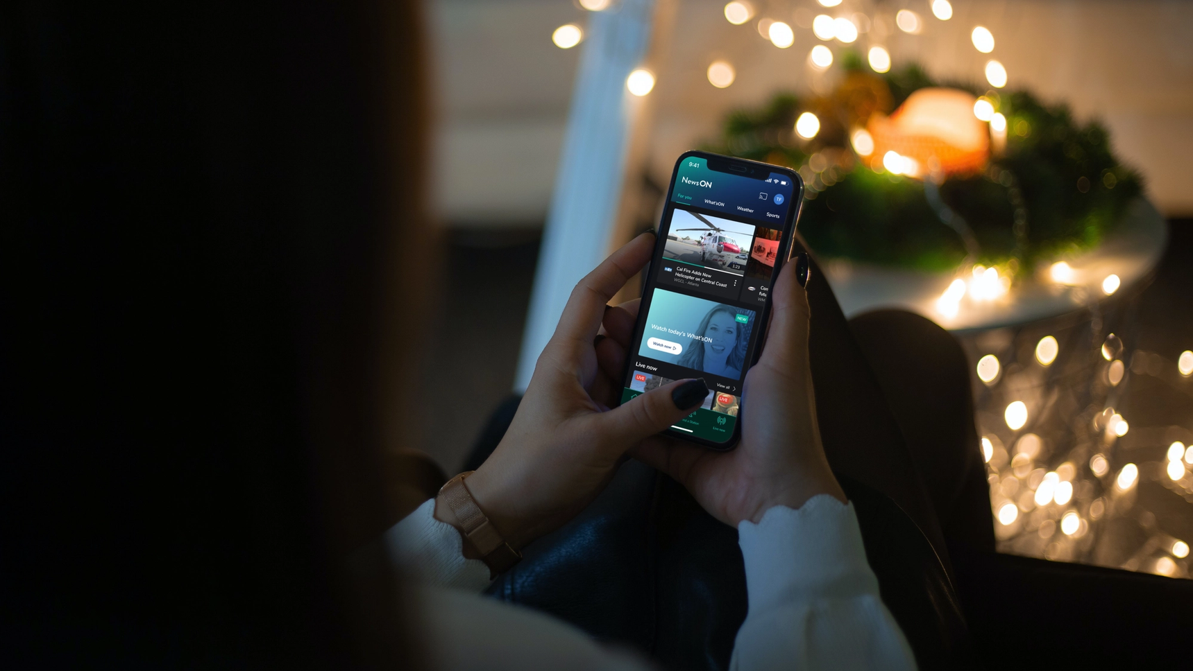 Back view of a woman holding a mobile device. The screen displays the mobile app home screen of NewsON consisting of news items.