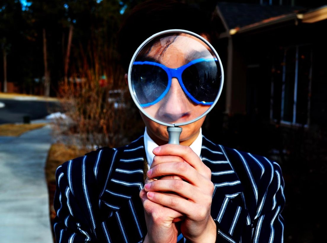 A man's face with glasses seen through a magnifying glass, used as the hero image for the article "It’s Called UX/UI! Look It Up!".