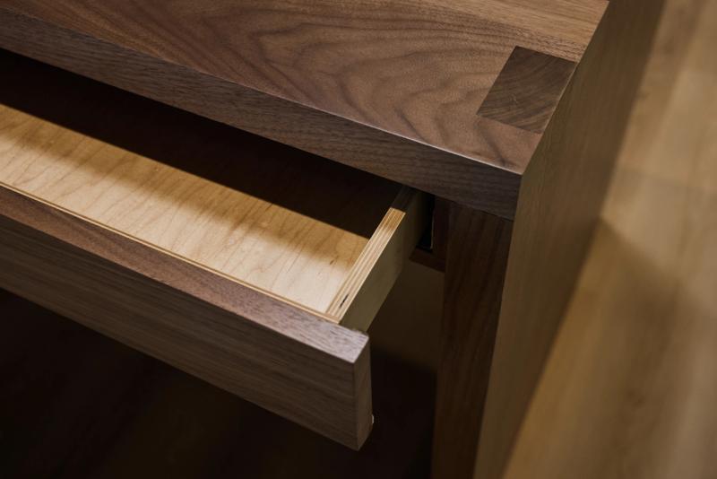 A close-up of an open walnut drawer on a custom dresser, revealing light maple interior construction and clean joinery details.