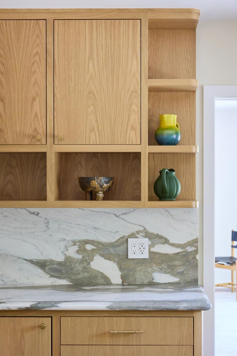Custom white oak kitchen cabinetry featuring open shelving with decorative ceramic vases, brass hardware, and a dramatic green and white marble countertop and backsplash.