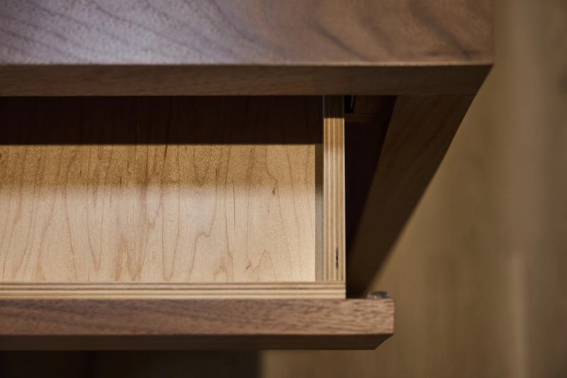 A close-up view of an open drawer box with a light maple plywood interior and dark walnut exterior frame, showing clean construction and soft-close hardware.